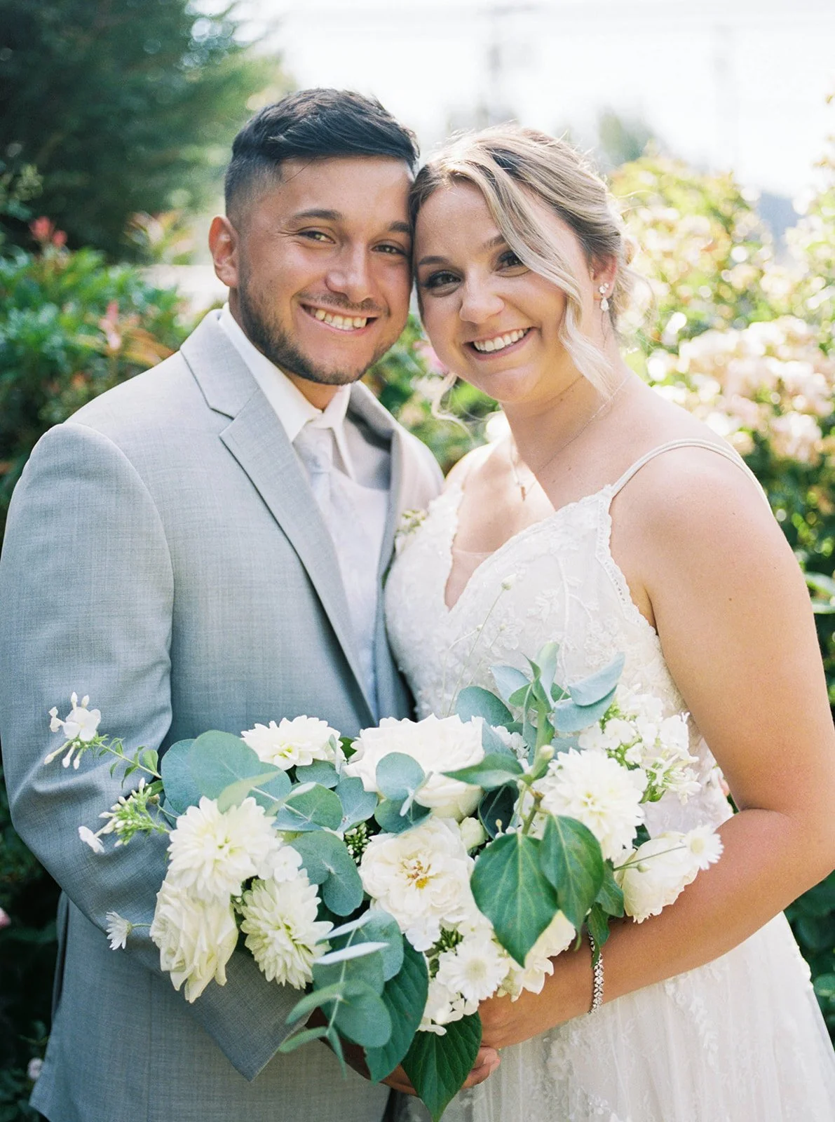 Newlyweds smiling with lush white bouquet in romantic garden wedding portrait at Abigail’s Garden.