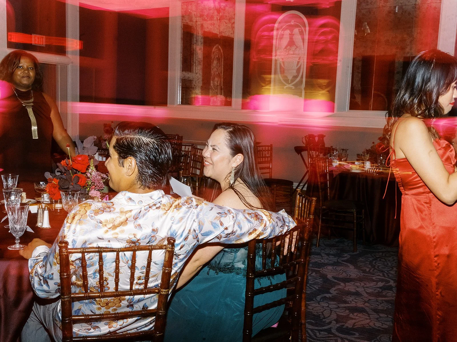 Guests seated together at reception table with motion blur and pink light streaks across the scene.