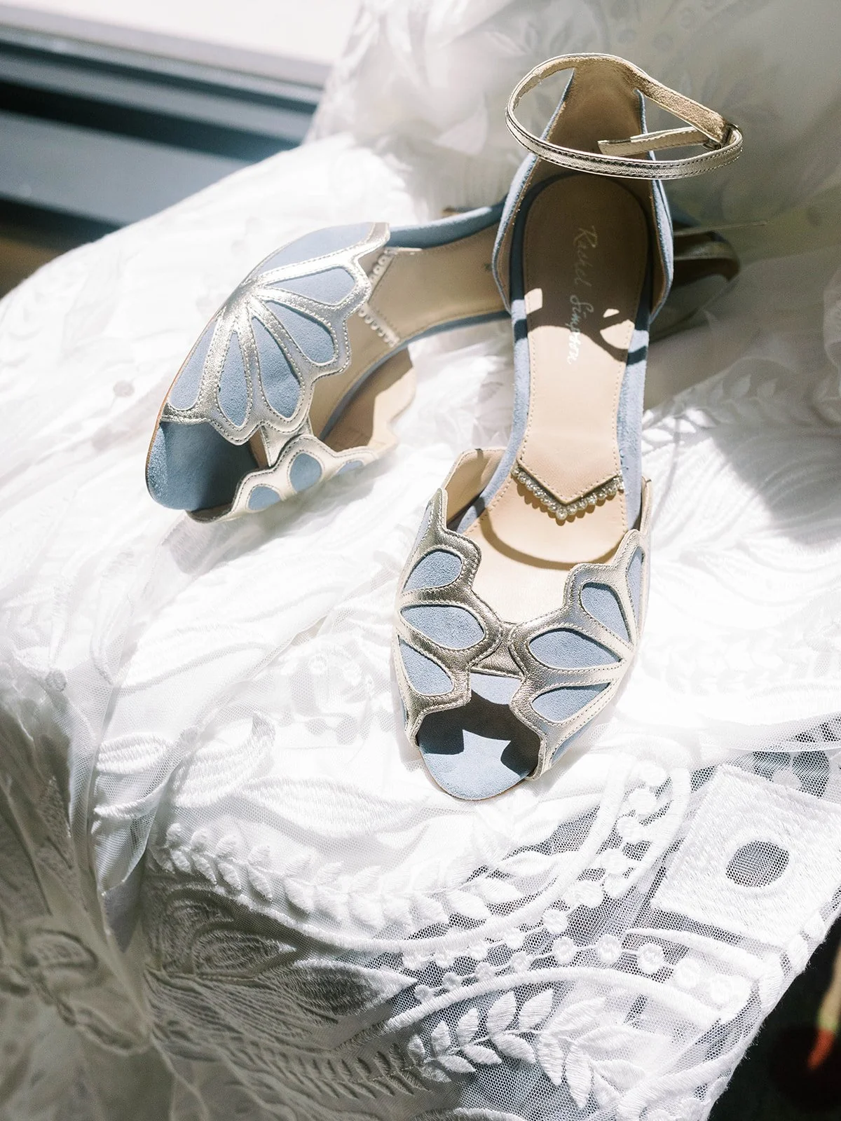 Blue and gold bridal shoes resting on lace wedding dress in soft natural light