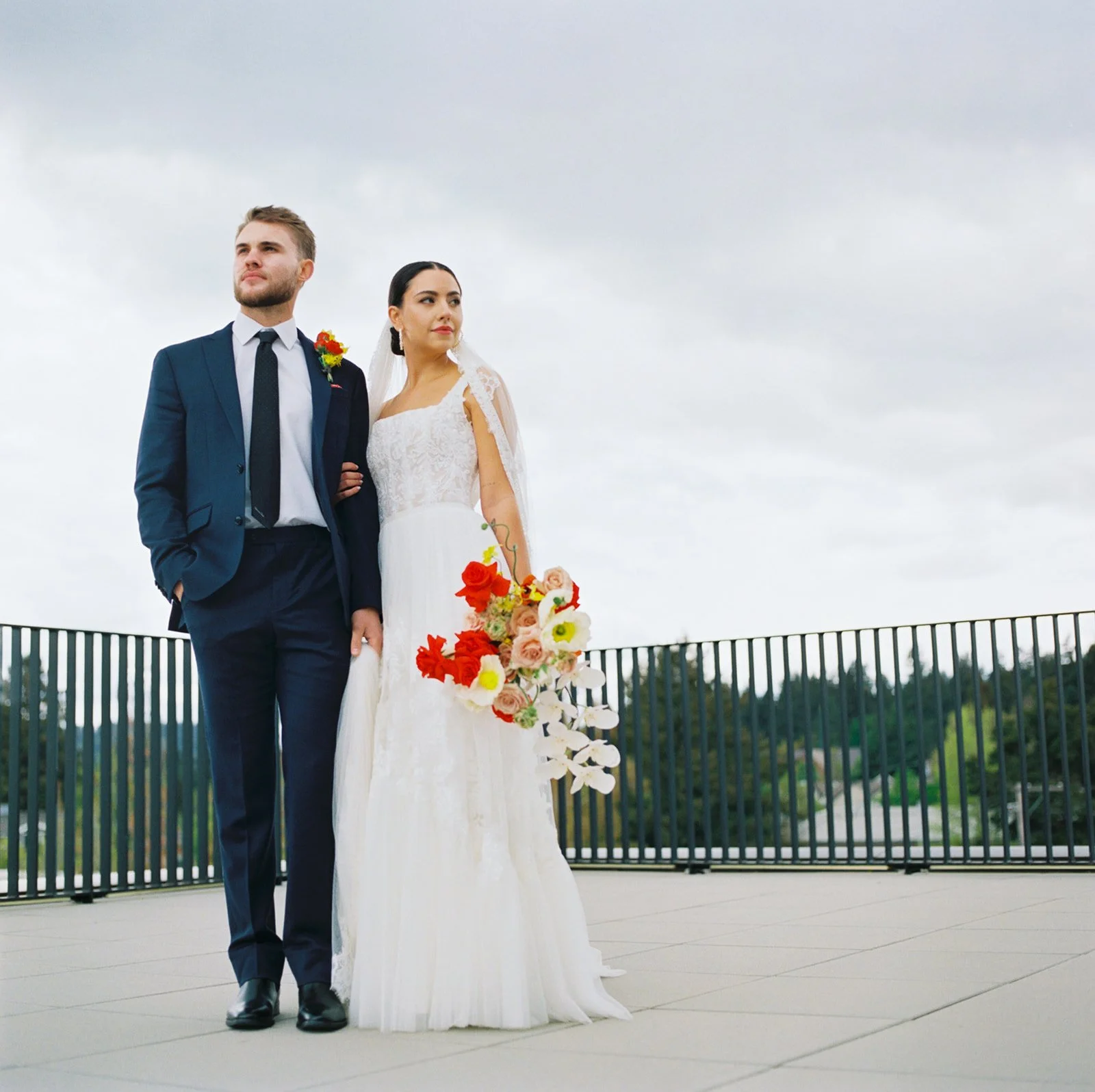 Bride and groom posing on the terrace at Ironlight with a colorful bouquet and Oregon landscape behind them.