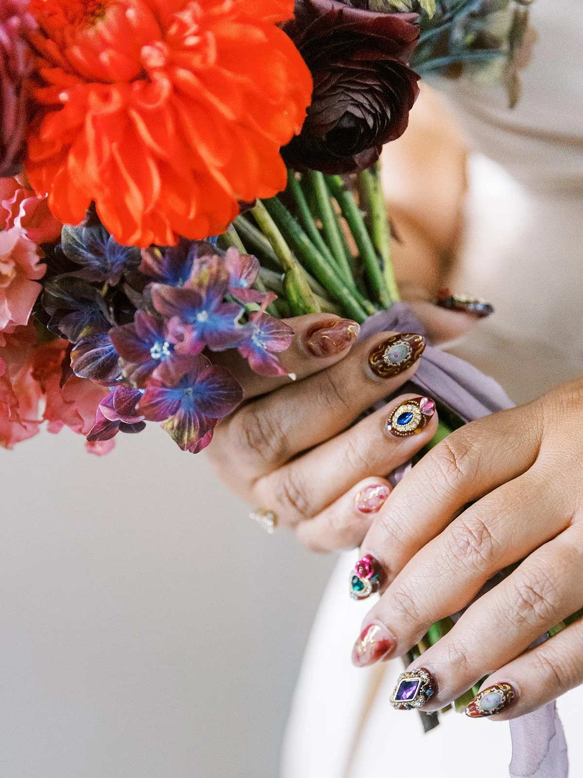 Close-up of colorful bridal bouquet with detailed nail art holding the stems.
