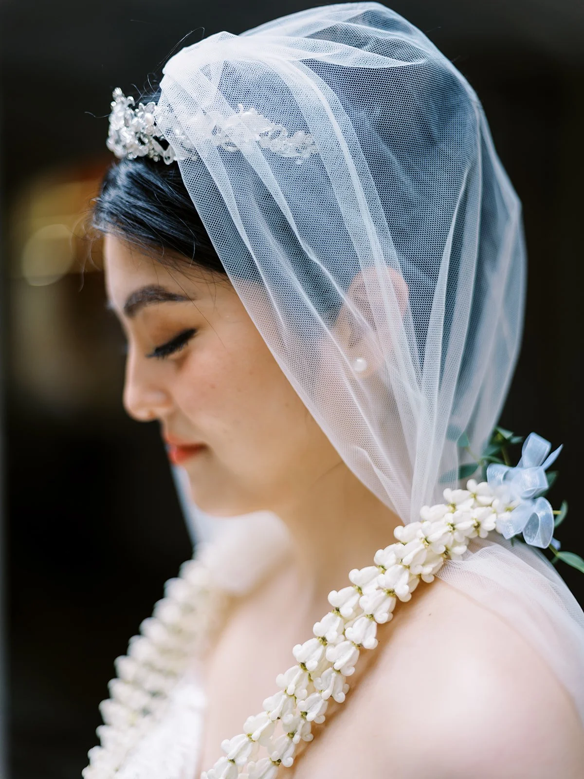 Close-up of a bride wearing a sheer veil, floral headpiece and white jasmine garlands.