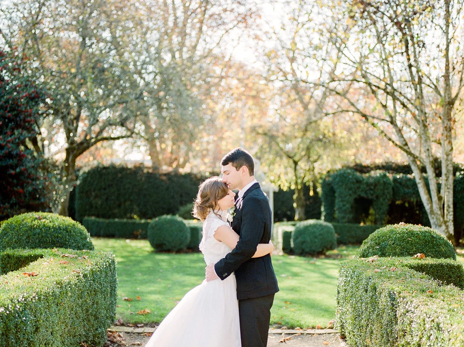 Bride and groom embracing among manicured hedges and trees at Deepwood Museum & Gardens in Oregon.