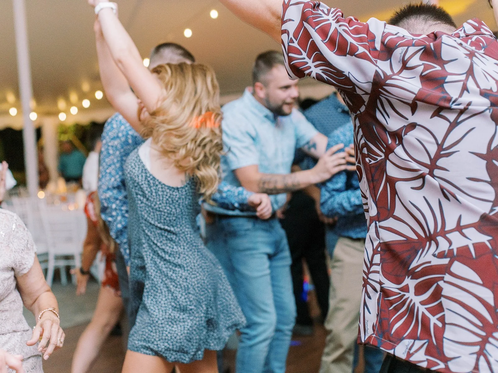 Wedding guests dancing under warm string lights at an outdoor tent reception.