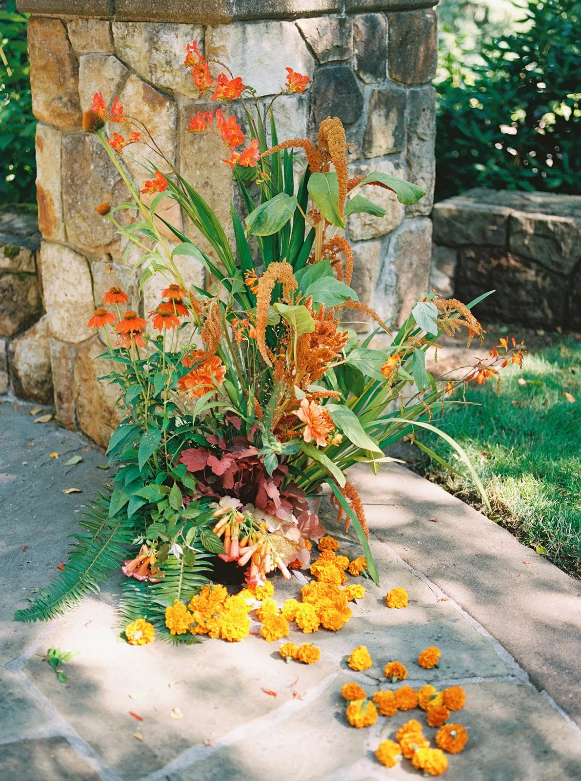 Colorful floral arrangement with orange blooms and greenery displayed beside a stone pillar.
