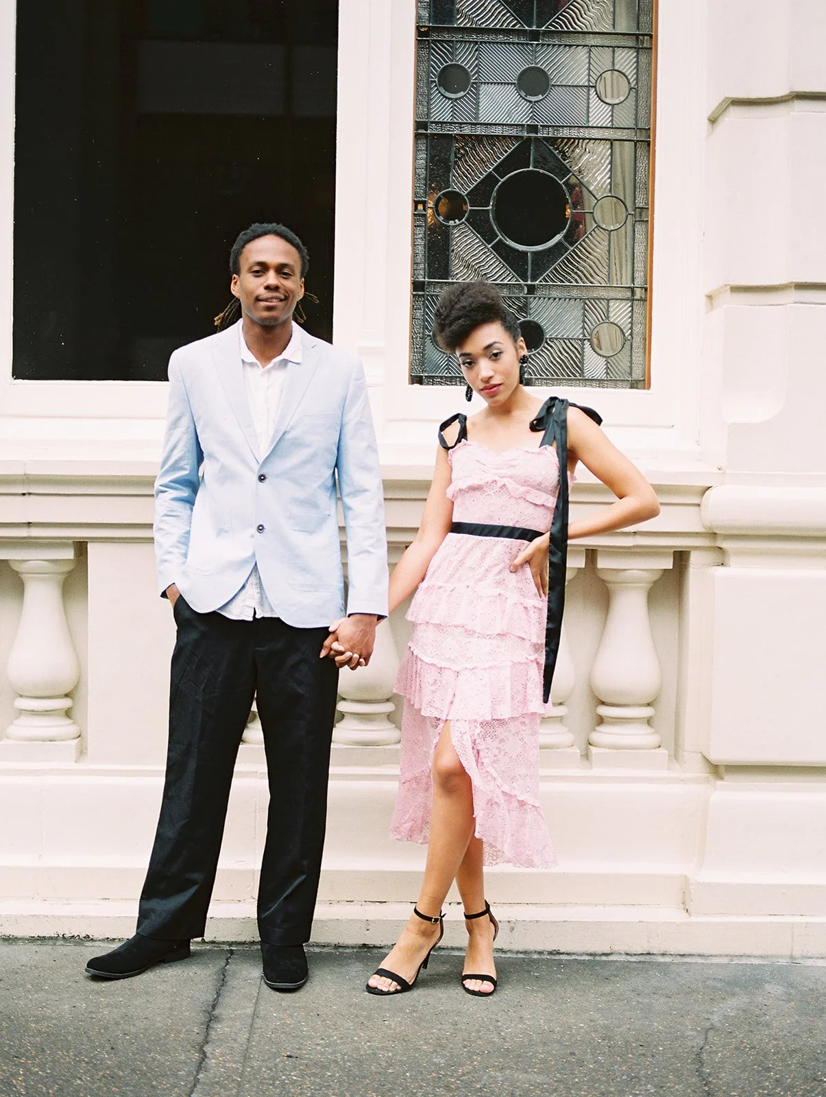 Couple posing together in front of decorative Portland building facade, holding hands