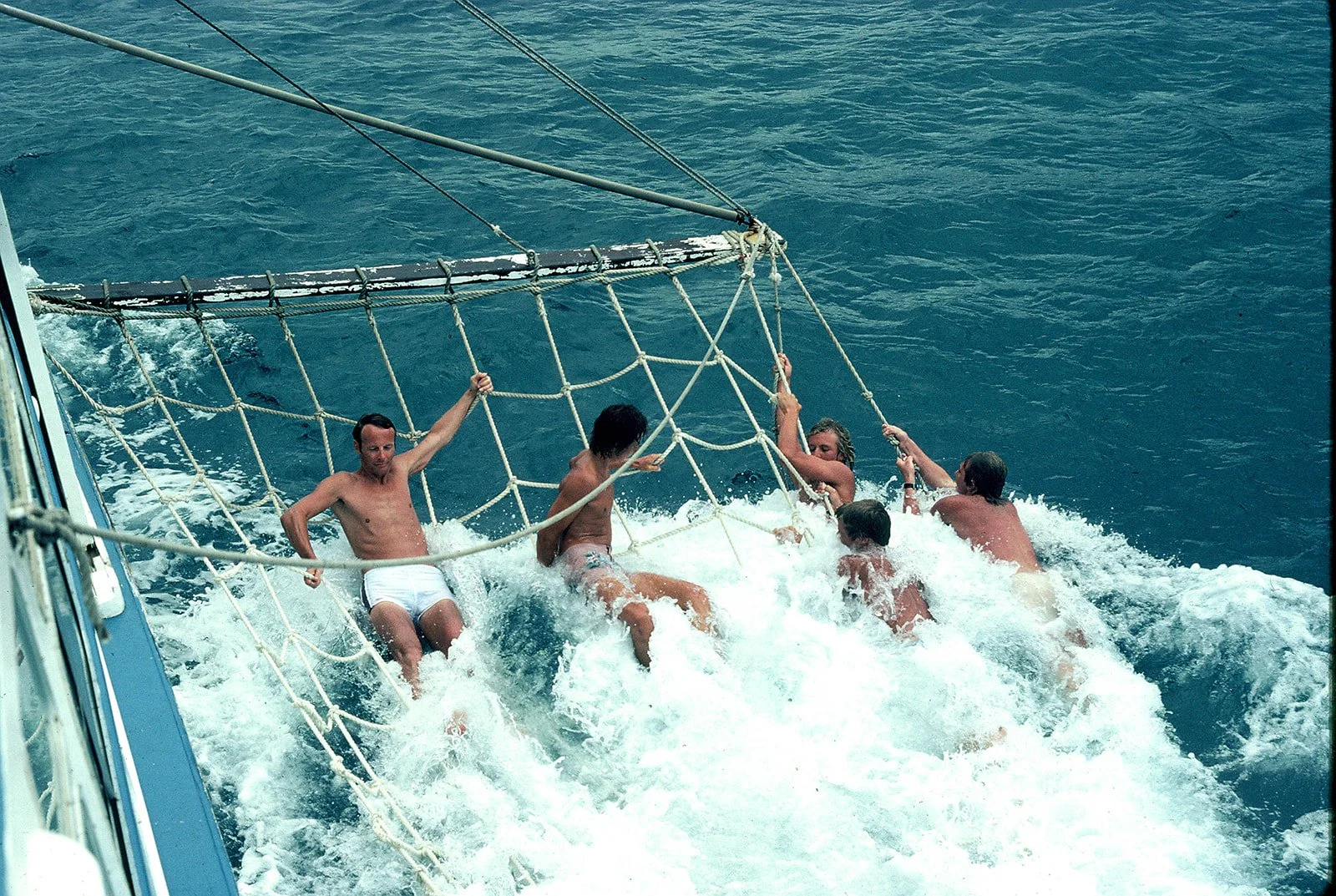 Group of people climbing from the water onto a boat using a rope net.