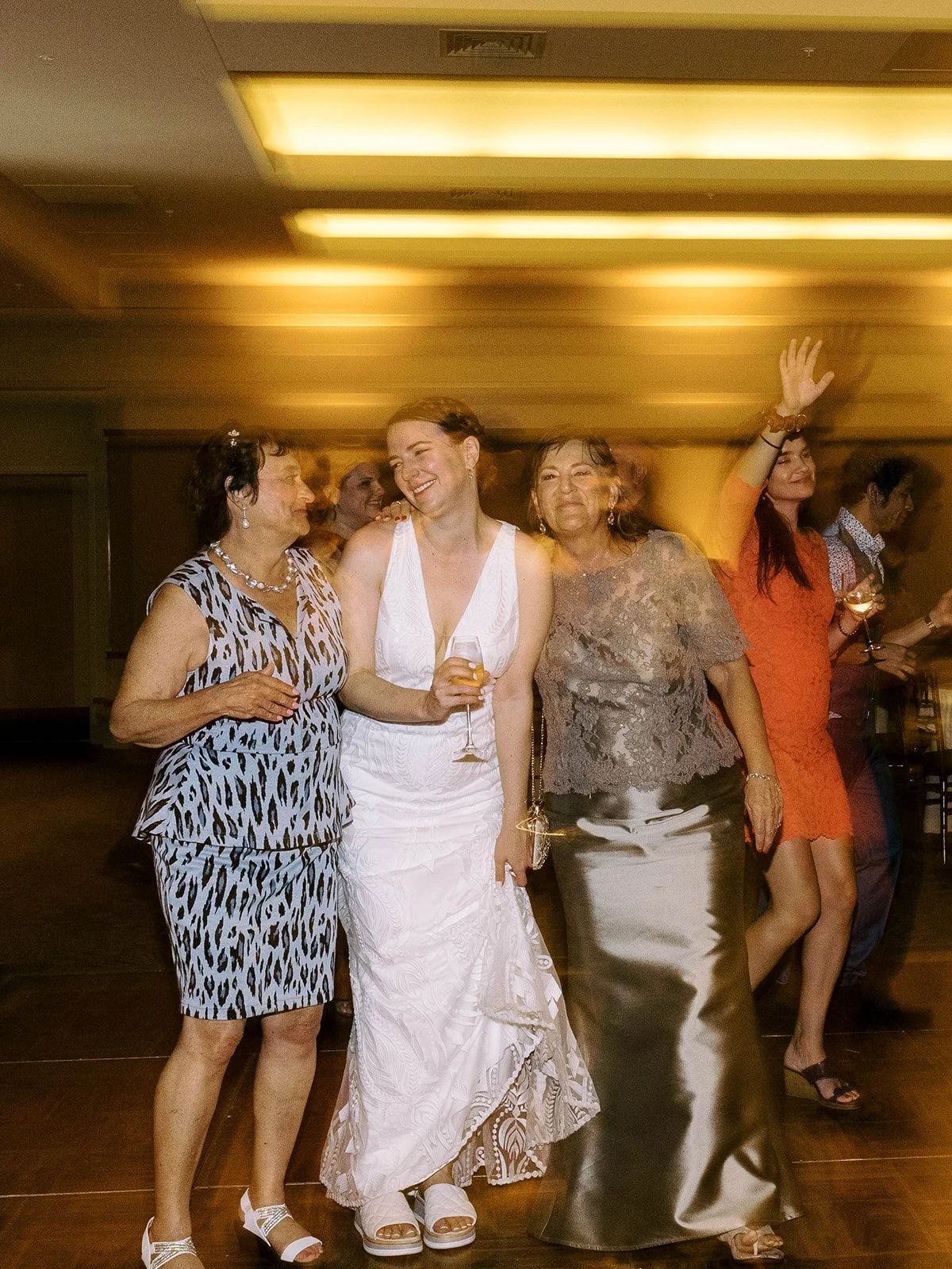 Bride standing between two wedding guests on the dance floor during the evening reception.