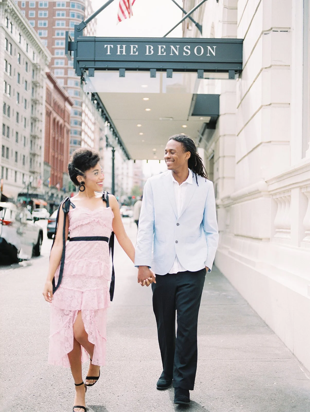 Couple smiling at each other while walking downtown Portland sidewalk near hotel entrance