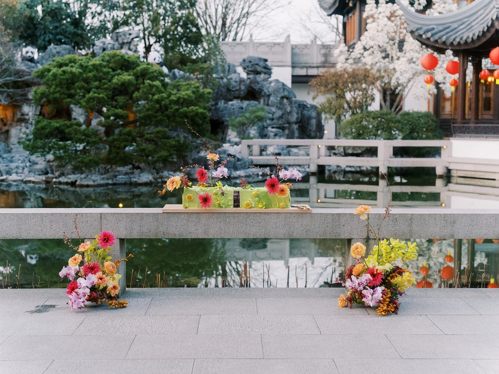 Colorful floral wedding arrangements displayed beside a pond in a traditional Chinese garden.