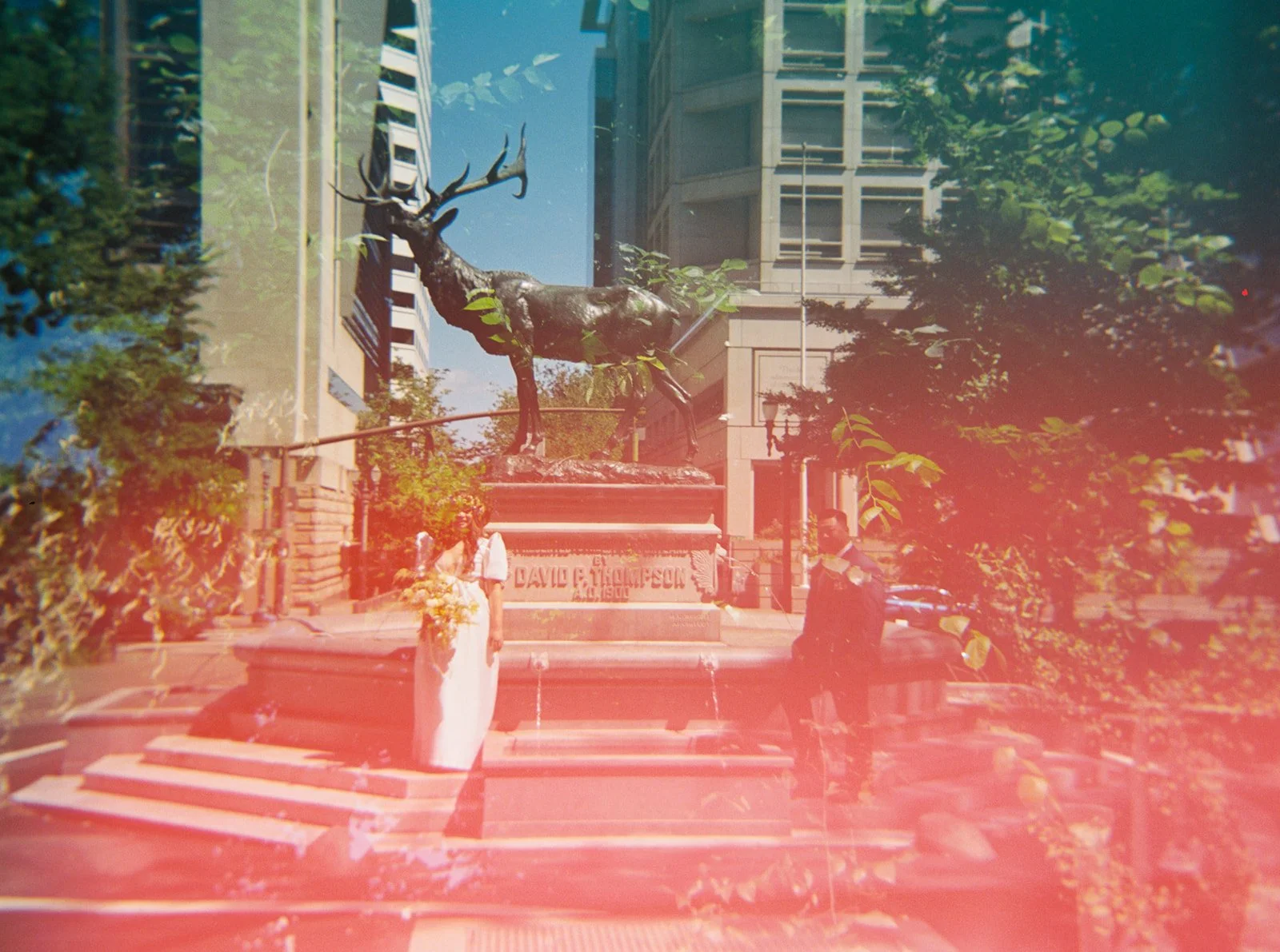 Bride and groom pose near the historic elk statue in downtown Portland, captured in a dreamy, light-leaked film photograph.