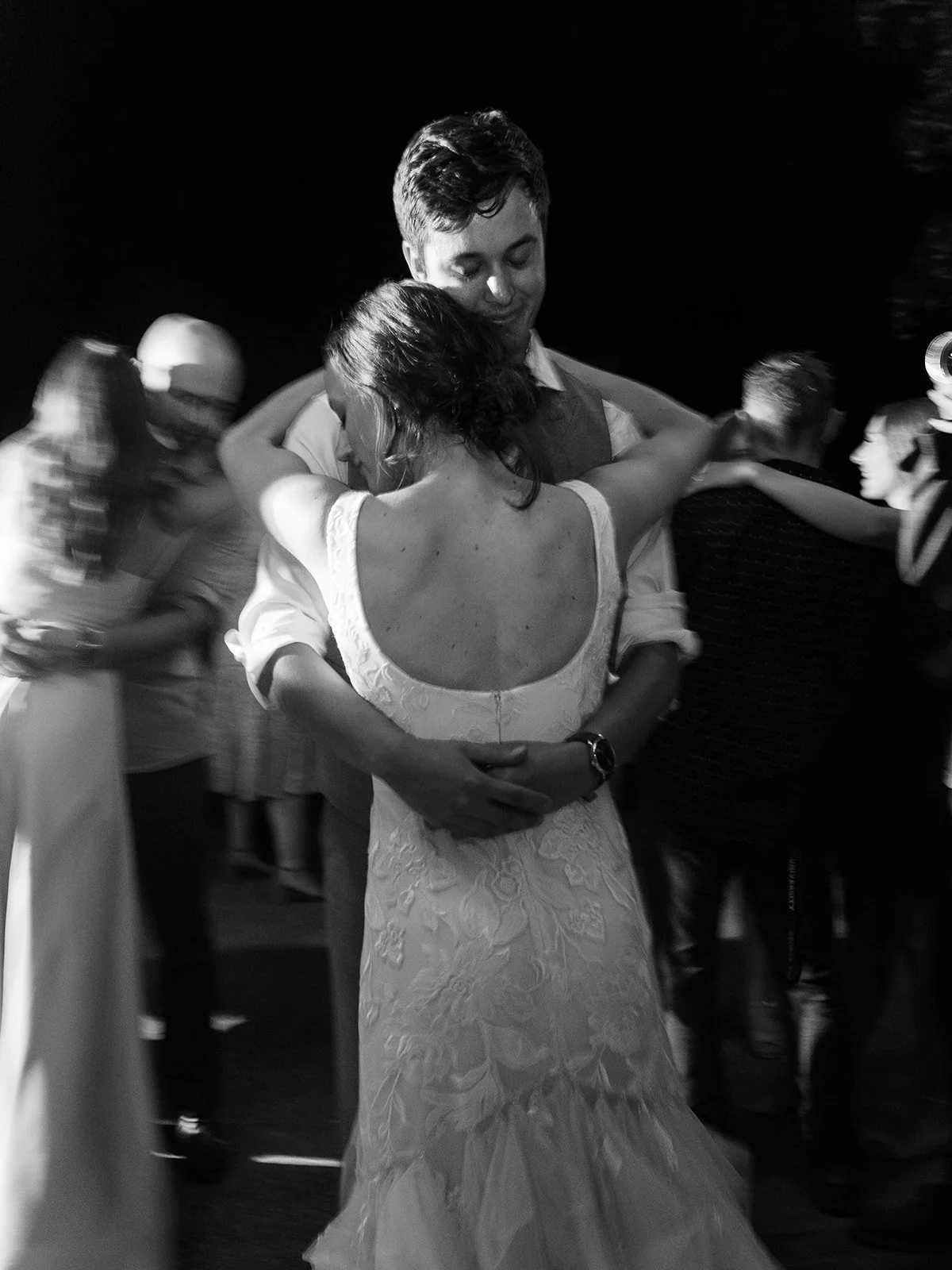 Black and white photo of couple slow dancing surrounded by guests on dance floor
