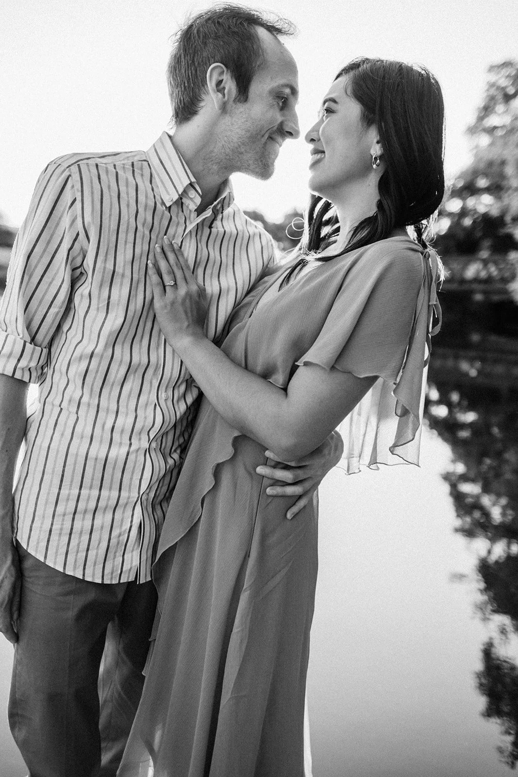 Couple embracing near the lake in black and white, soft reflections behind them