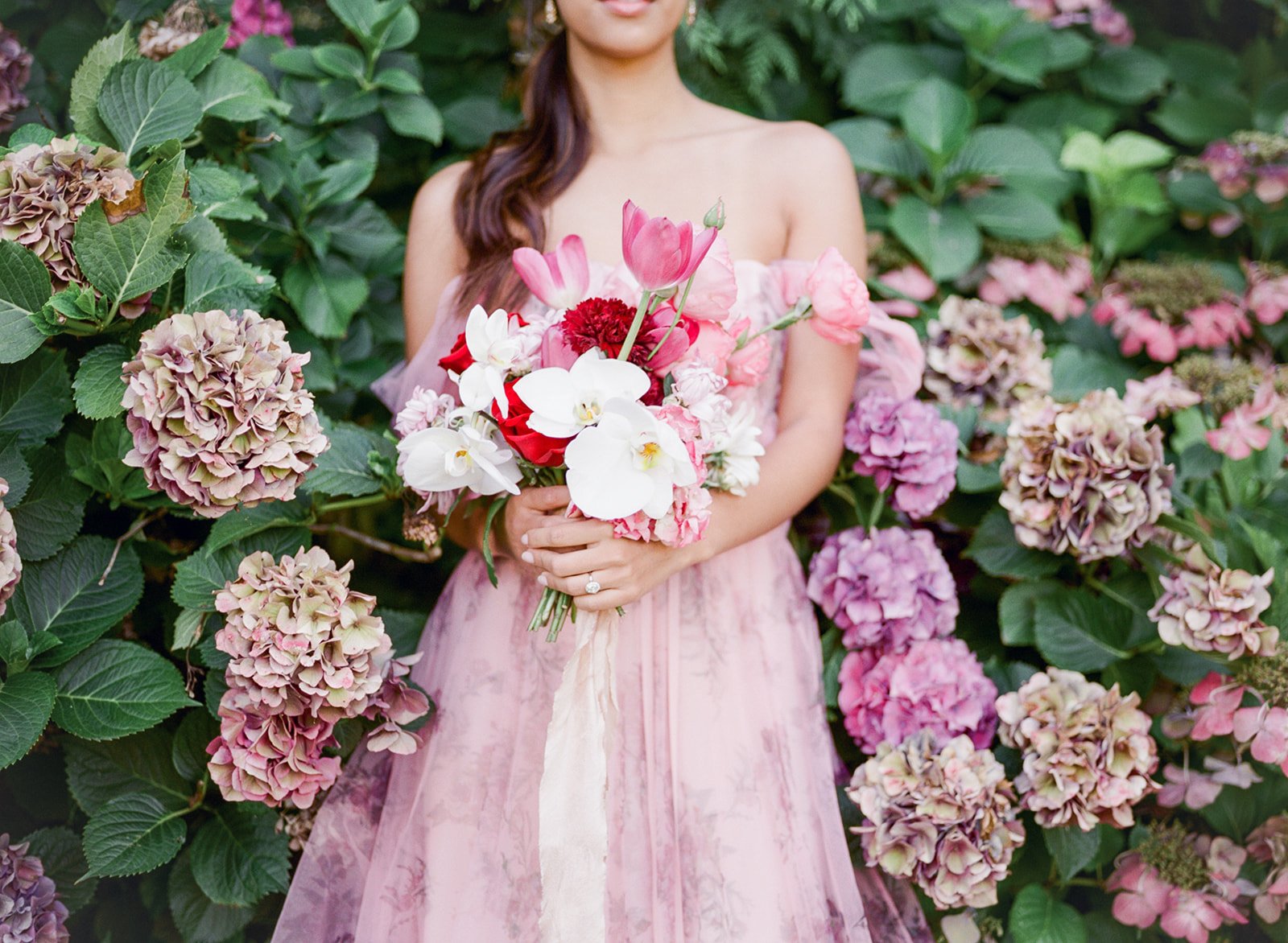 Bride holding pink and white bouquet in front of hydrangea flowers at Cathedral Park.