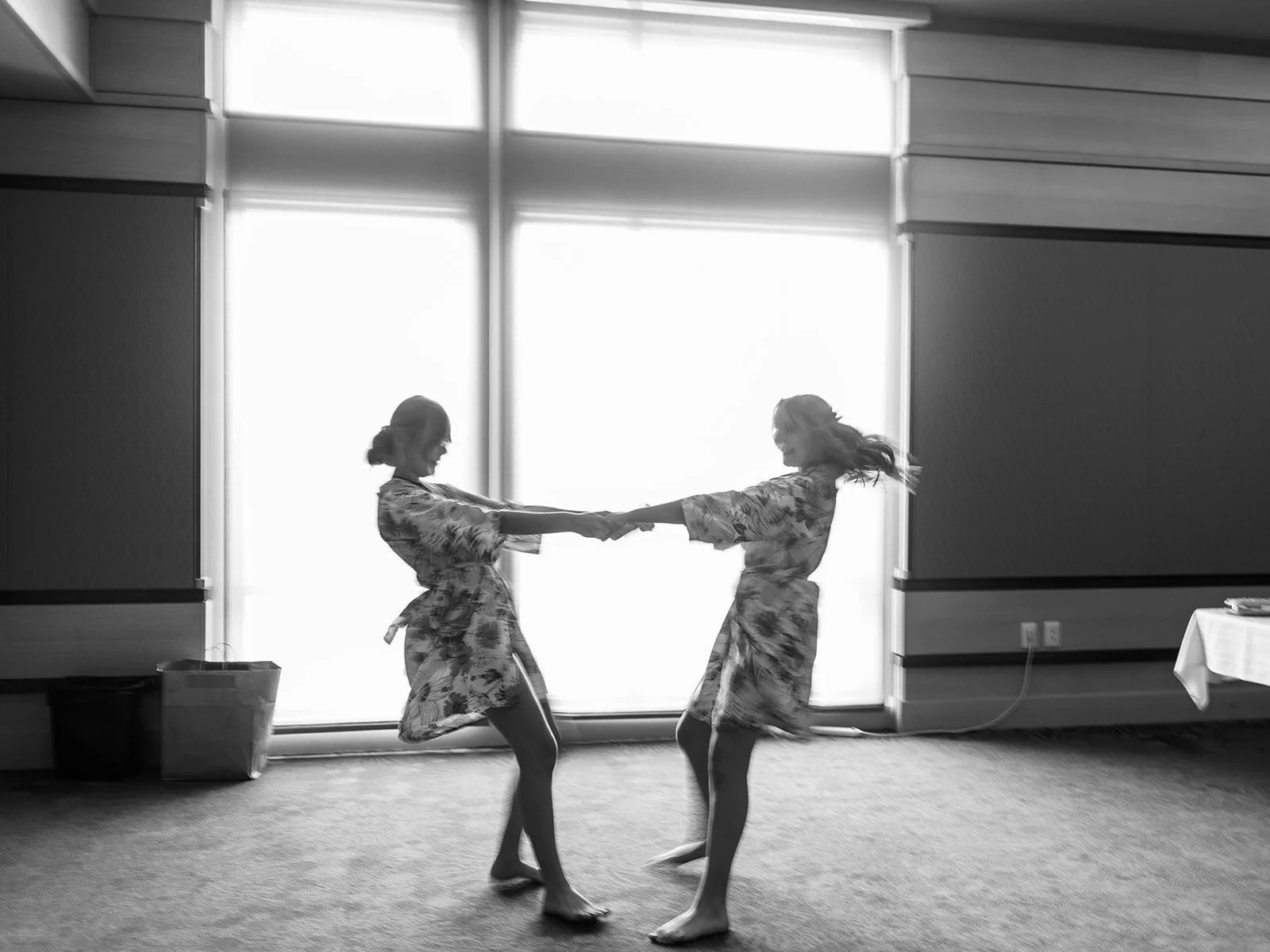 Two women in robes spinning and holding hands in front of bright window, black and white photo