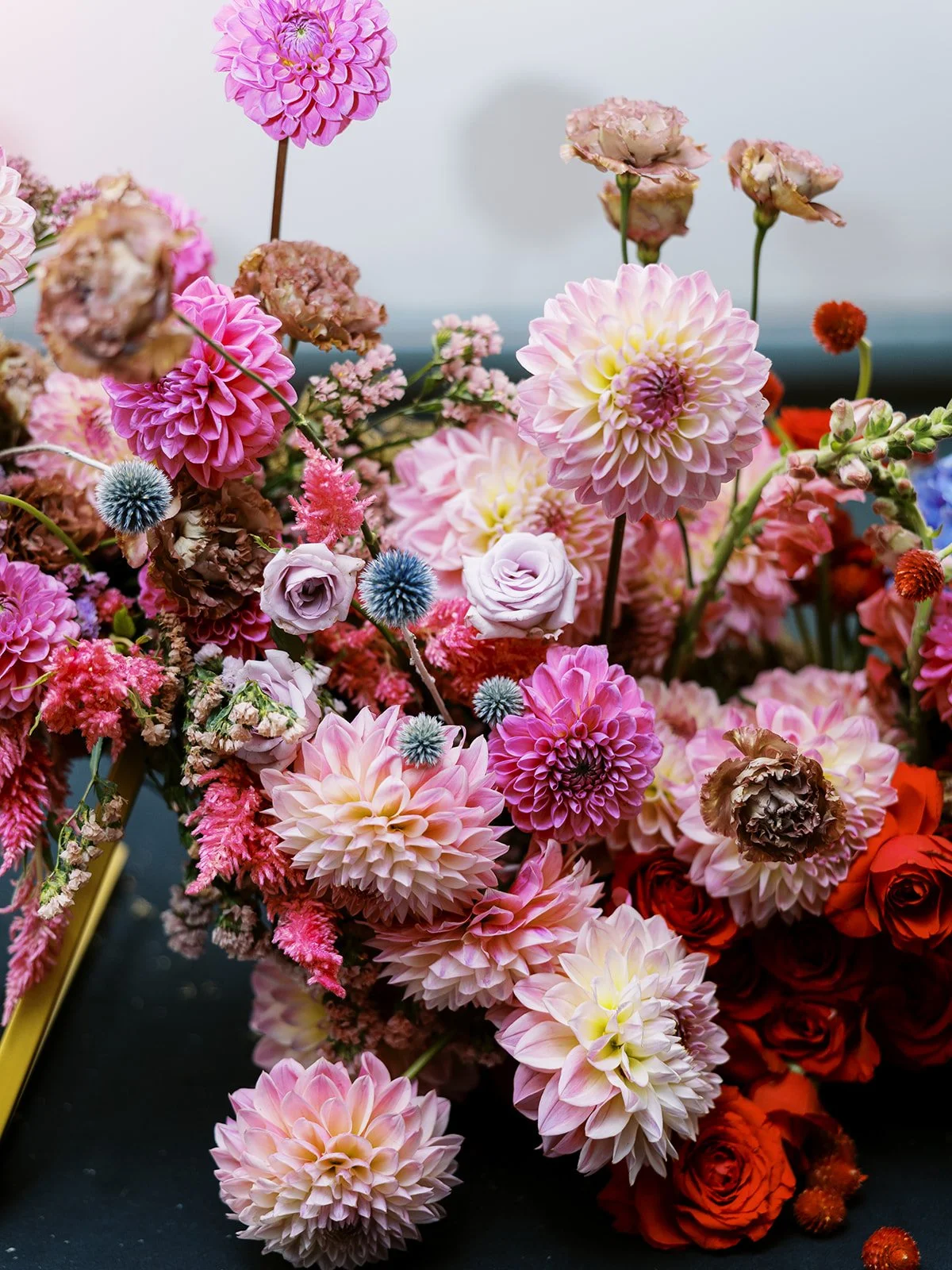 Lush arrangement of pink dahlias, roses, and textured blooms in soft blush and coral tones on a dark surface.