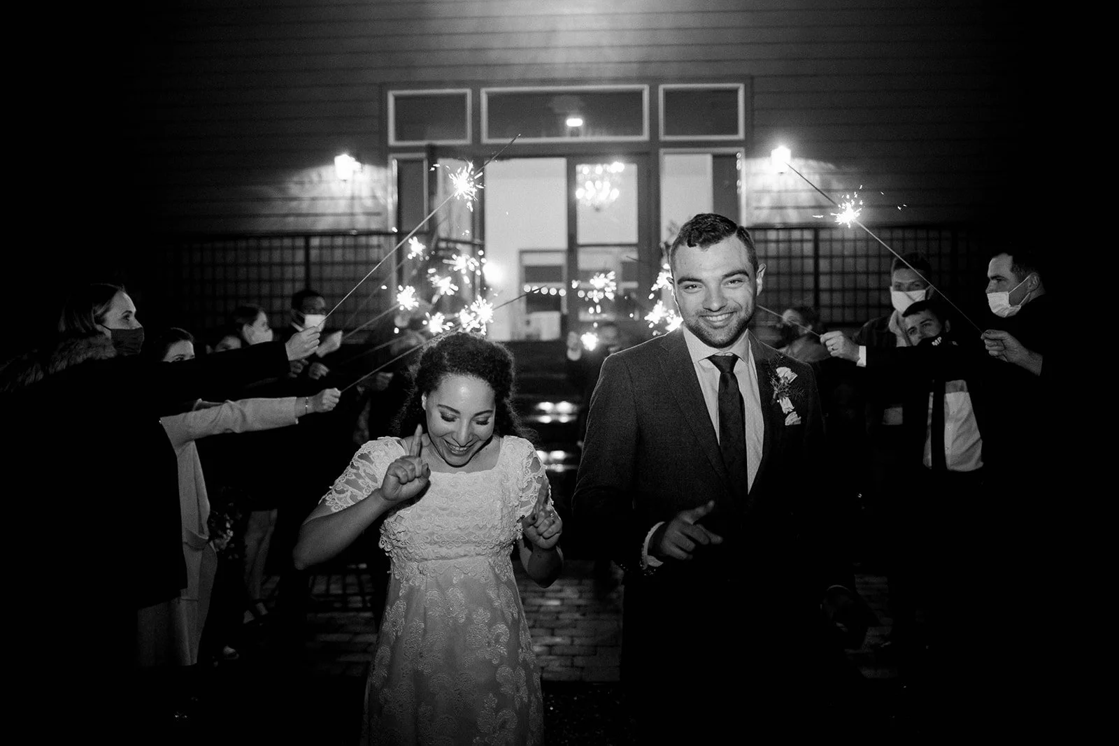 Black-and-white photograph of the newlyweds running through a sparkler exit at the end of their wedding.