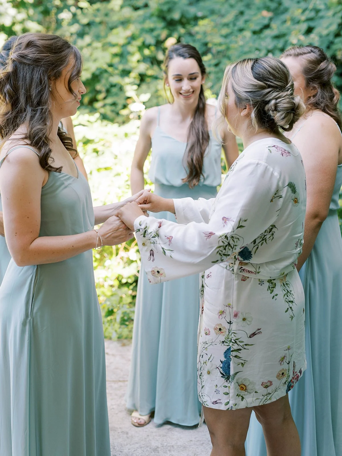 Bride sharing a quiet moment with bridesmaids in sage blue dresses before garden ceremony.