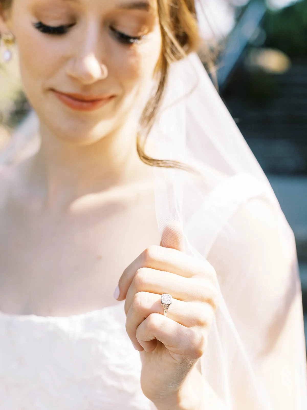Close-up of bride holding veil, showing engagement ring and soft natural light on her face.