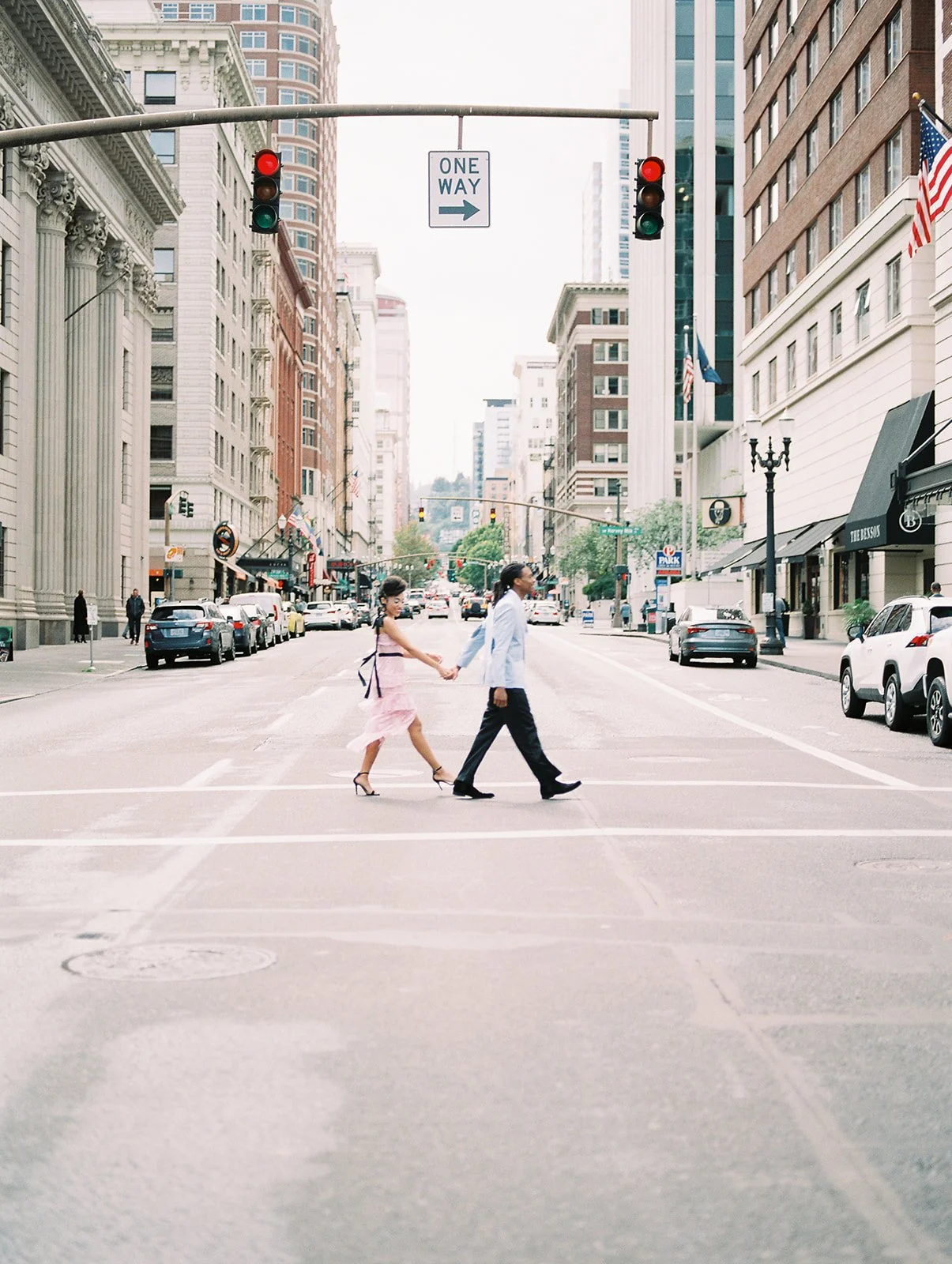 Couple holding hands crossing a city intersection in downtown Portland with traffic lights overhead