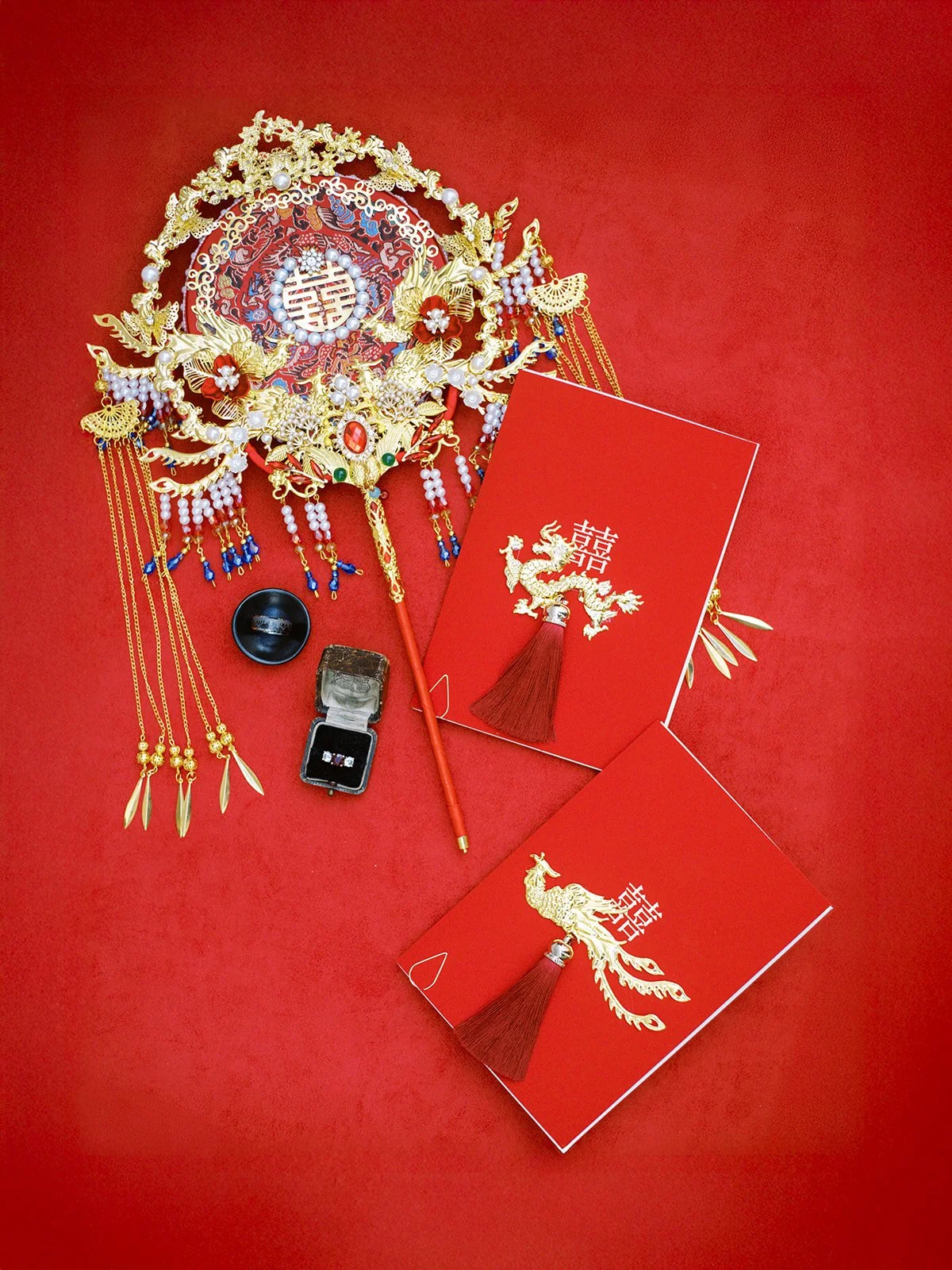 Traditional Chinese wedding accessories arranged on red background with ornate gold headpiece, red envelopes, and rings
