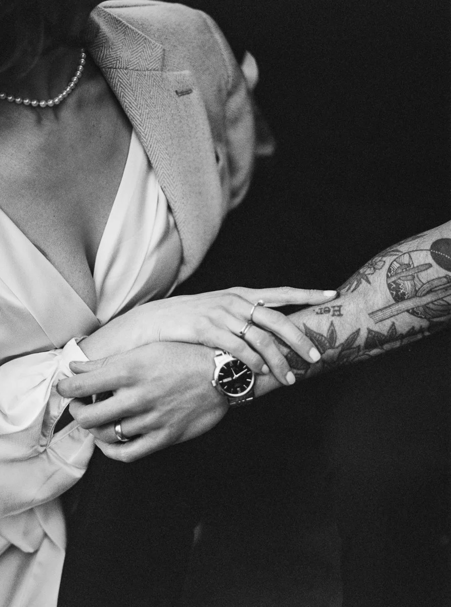 Black and white detail of couple’s hands and arms, engagement ring visible, man with tattoos and wristwatch