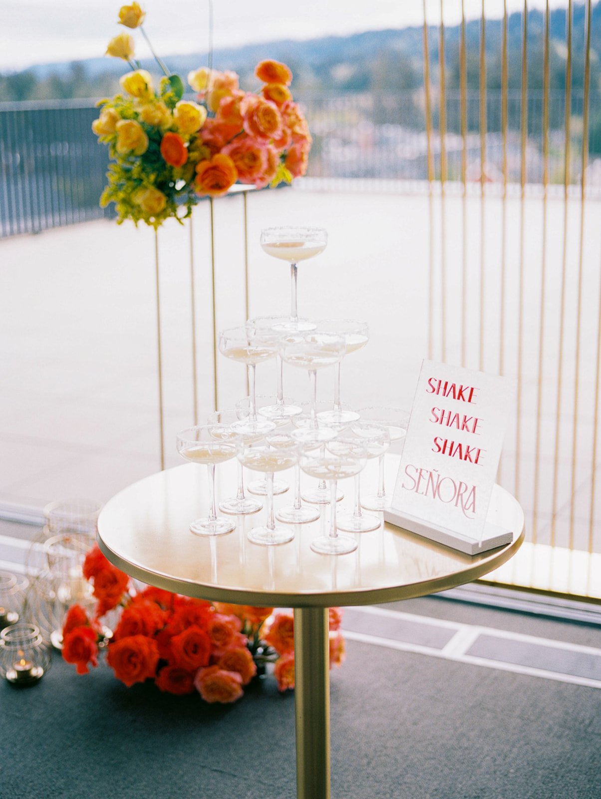 Champagne coupe tower displayed with bright orange wedding flowers and a ‘Shake Shake Shake Señora’ sign.