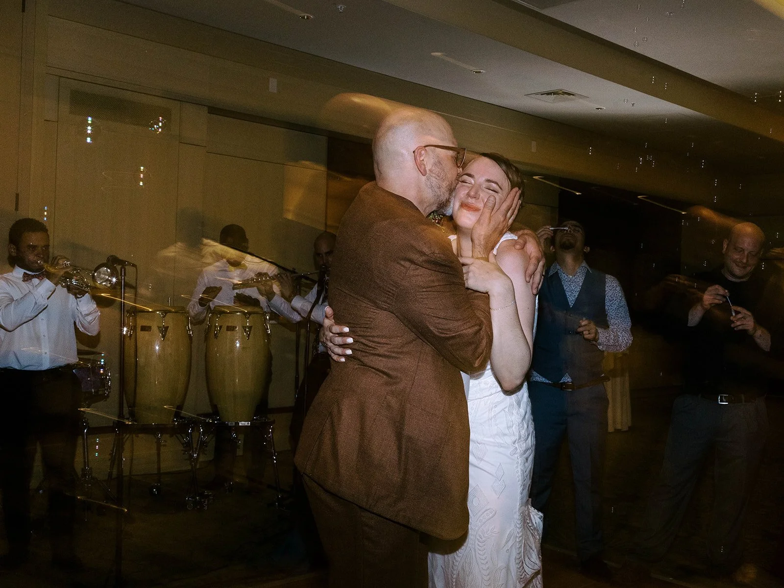 Groom tenderly cupping the bride's face for a kiss on the dance floor, with the live band and guests visible in the backgrou
