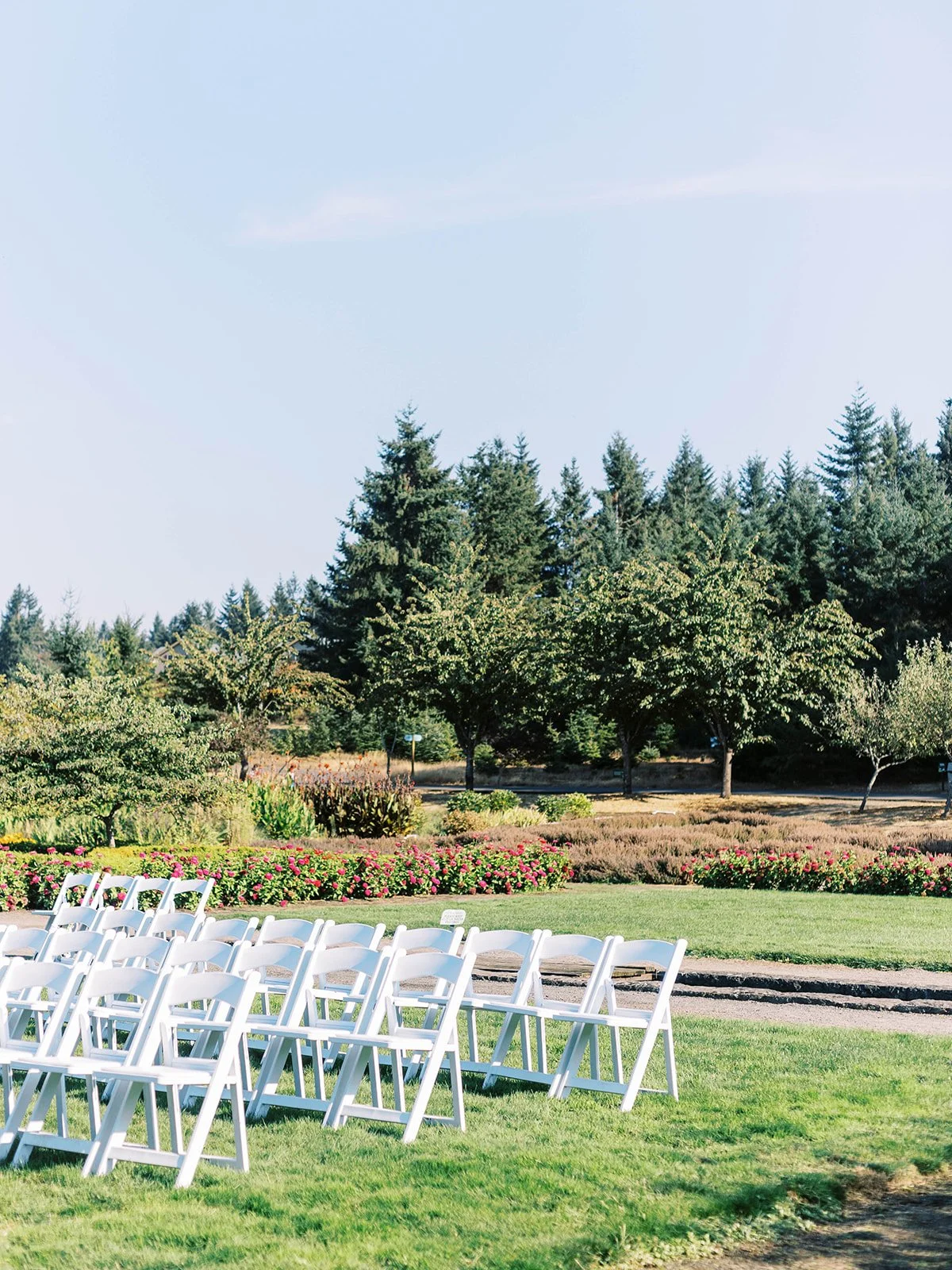 Outdoor wedding ceremony setup with white chairs on grass and garden backdrop