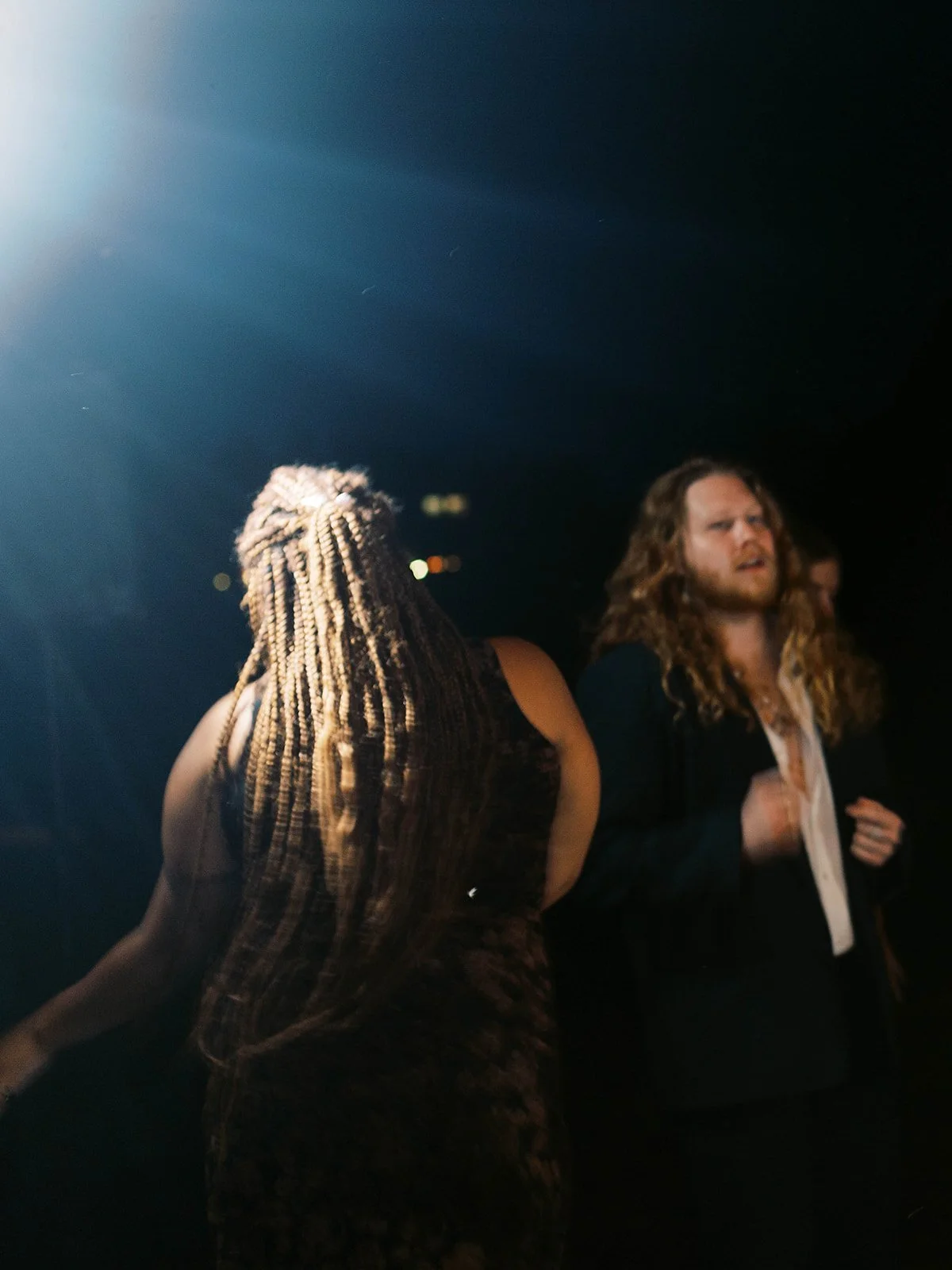 Guests dancing at night under spotlight during outdoor wedding reception with dark background