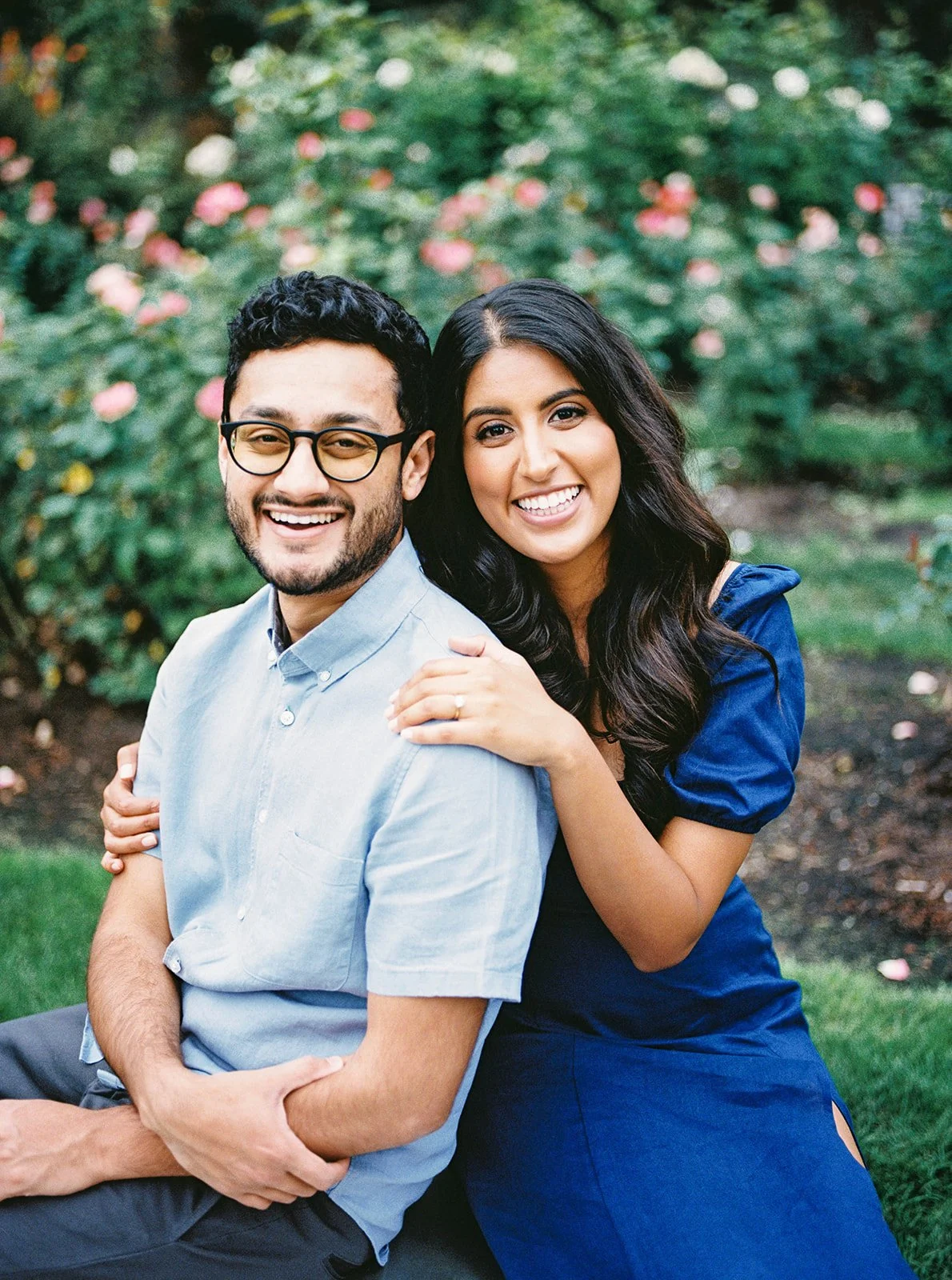 Engaged couple smile together among blooming roses during their Portland engagement session.