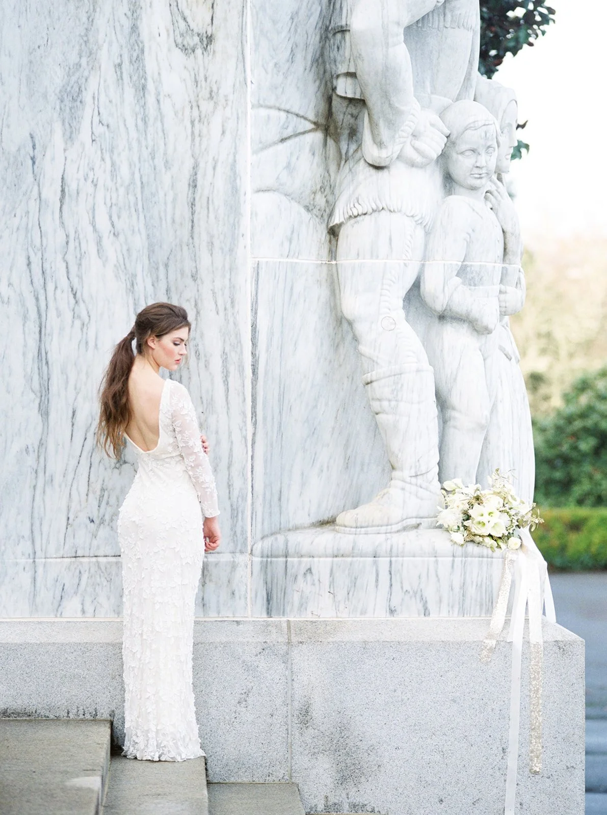Bride in a white lace wedding dress beside carved white stone architecture