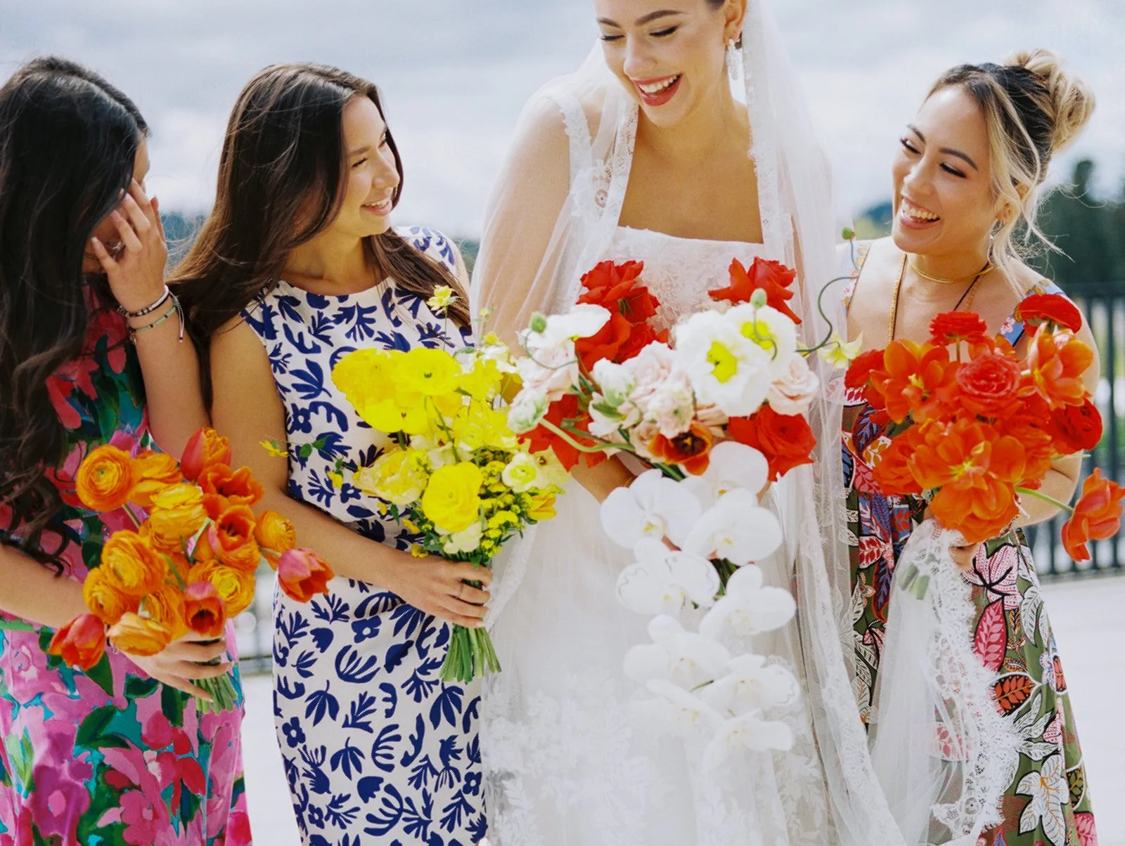 Bride in lace gown with bridesmaids in patterned dresses holding bright bouquets at Ironlight rooftop wedding