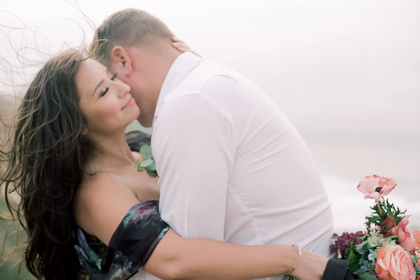 Close-up of man and woman embracing near the coast with soft, airy tones
