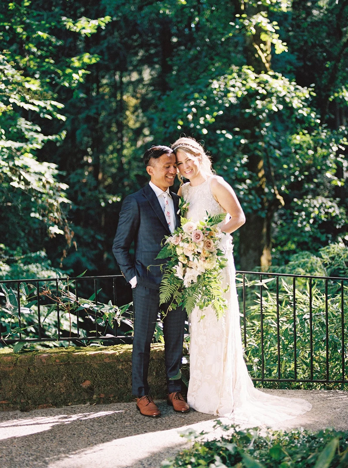 Bride and groom pose together among lush greenery with her cascading bouquet.