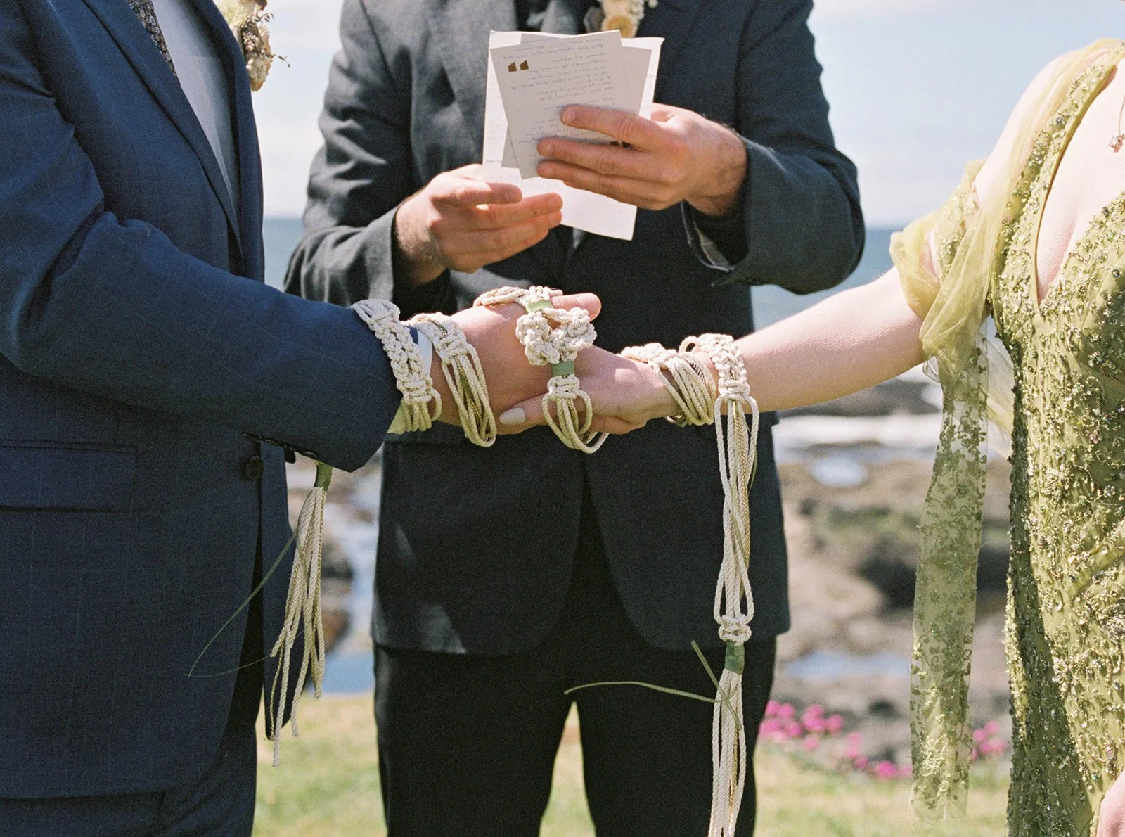 Couple’s hands joined with decorative cords during an outdoor wedding ceremony.