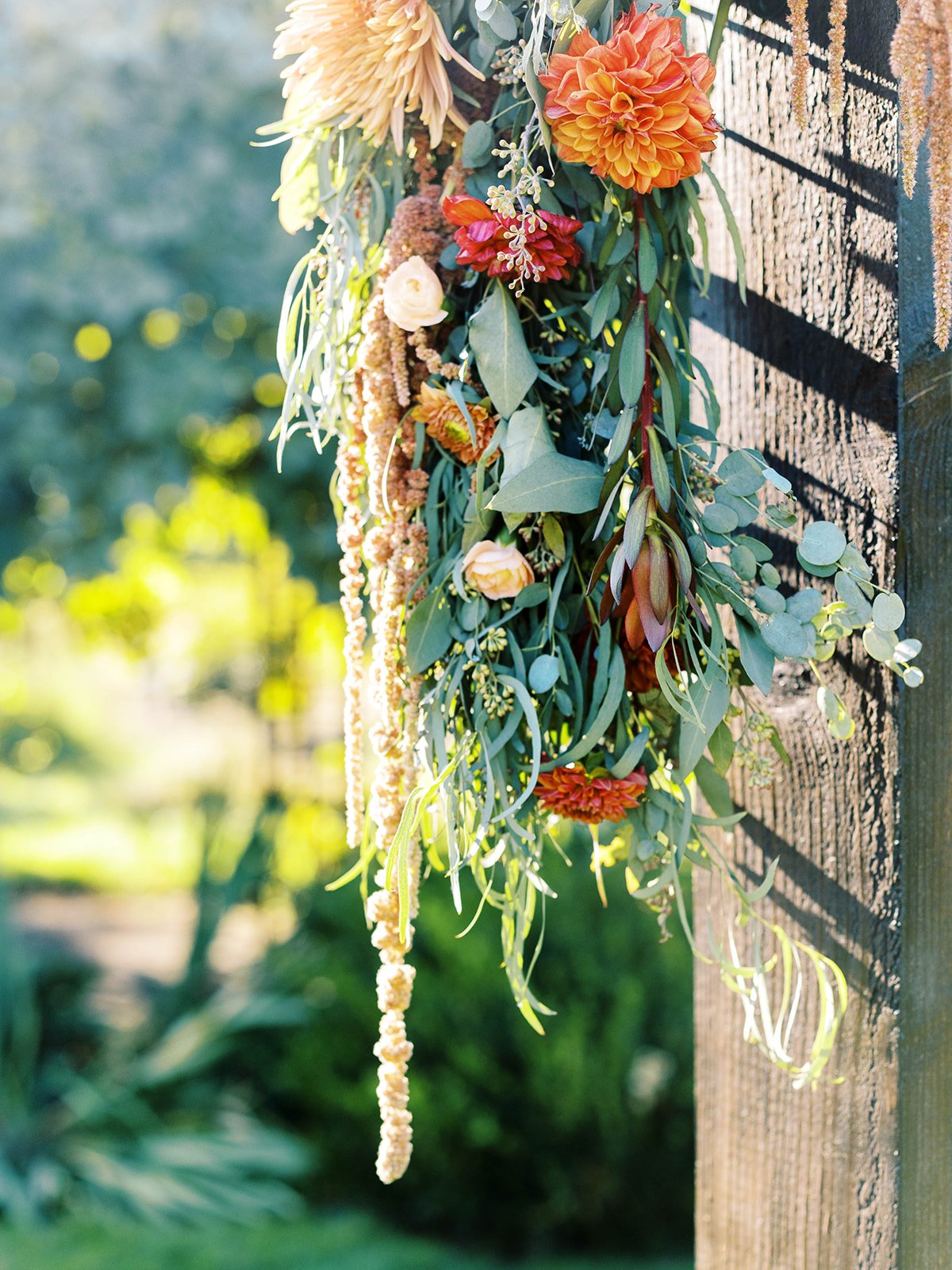 Orange, cream and rust flowers with trailing greenery decorating a dark wooden ceremony structure.