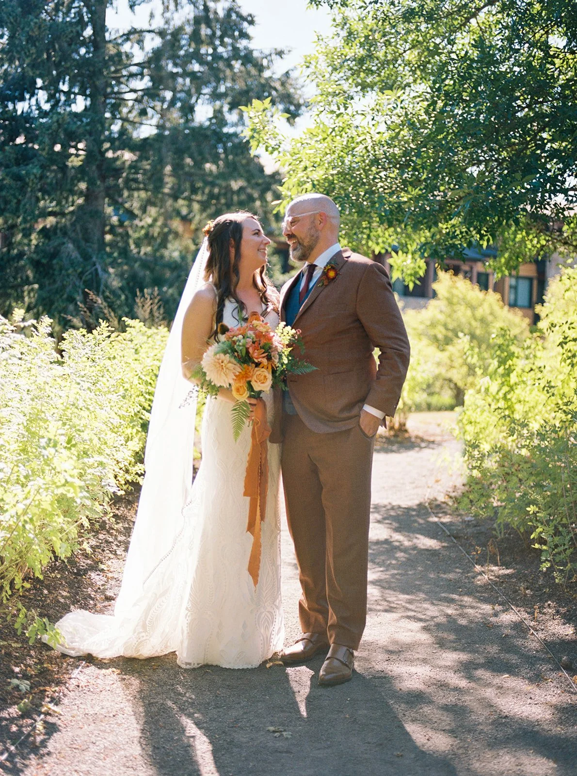 Bride and groom standing together on a sunlit garden path at The Allison Inn, surrounded by lush greenery.