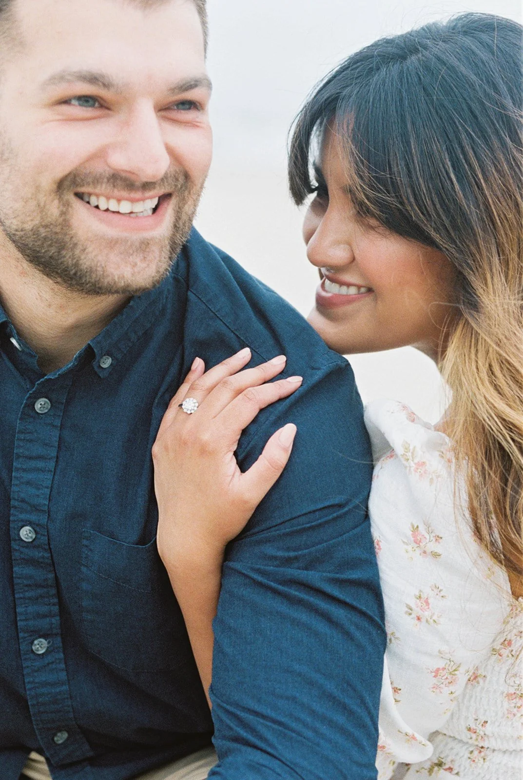 Close-up of couple smiling together, woman’s hand with engagement ring resting on man’s shoulder