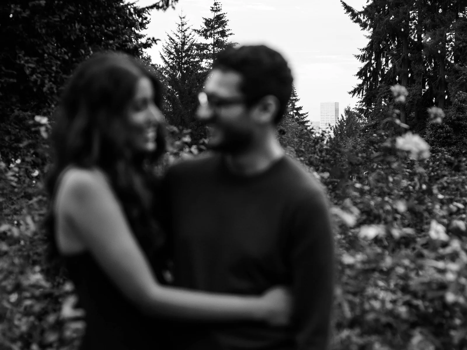 Soft-focus black-and-white portrait of an engaged couple embracing among the rose bushes.