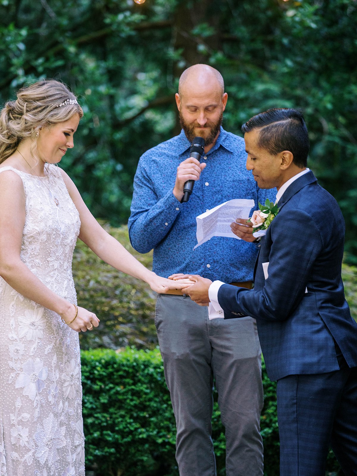 Groom holds the bride’s hand during the ceremony while the officiant reads behind them.