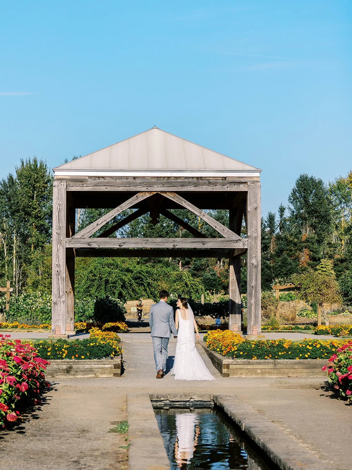 Newlyweds walking away under wooden pavilion surrounded by flowers and garden paths