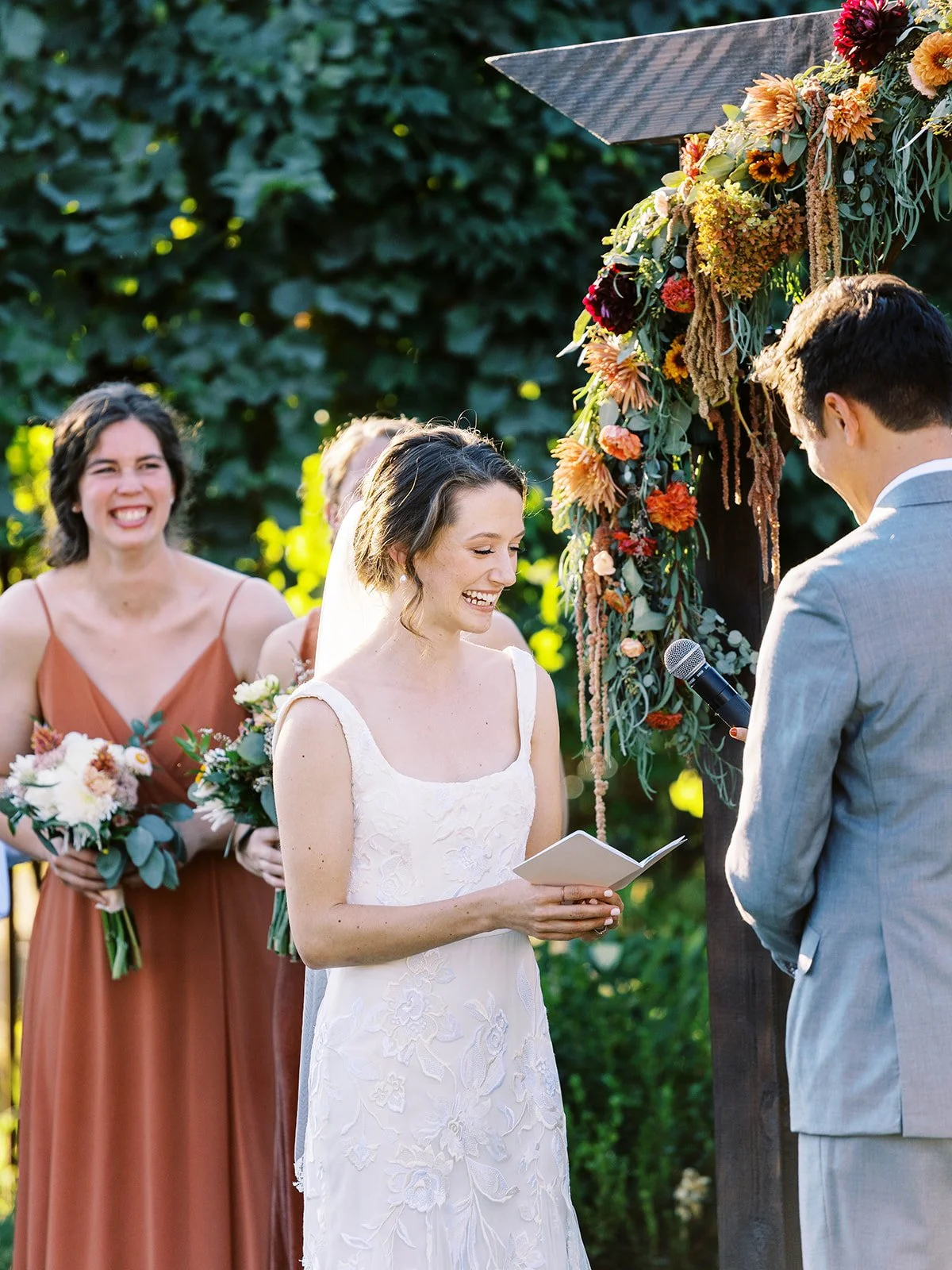 Bride reading vows during outdoor wedding ceremony under wooden arch with floral arrangement