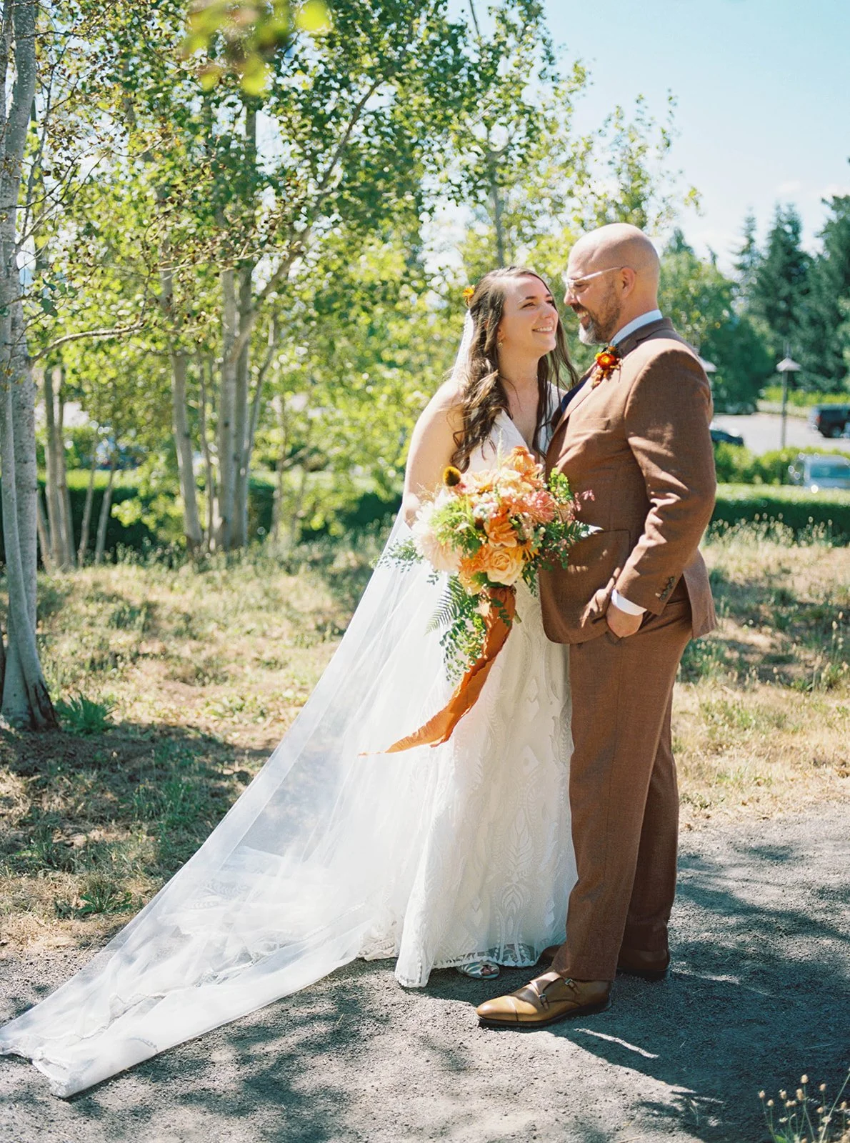 Bride and groom standing together on path, holding bouquet in sunny vineyard setting