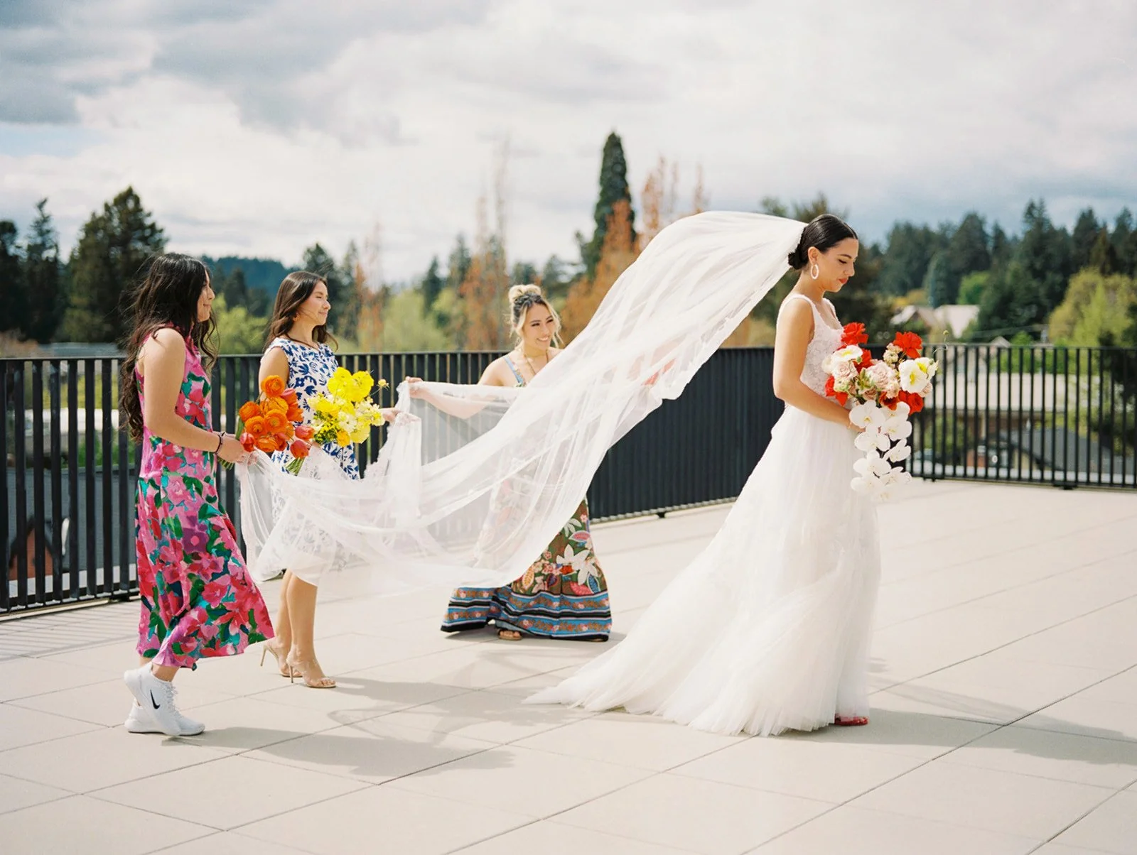 Bride walks with her colorful wedding party as they carry her long veil at an Oregon wedding