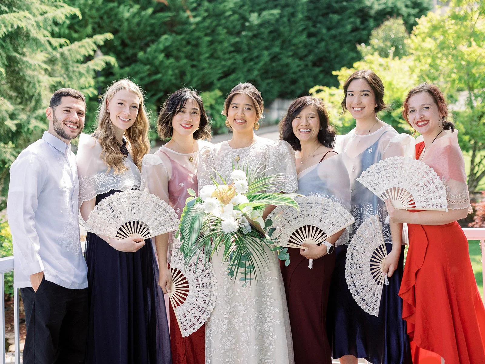 Bride and wedding party posing with white lace hand fans and a tropical bouquet in a lush garden

