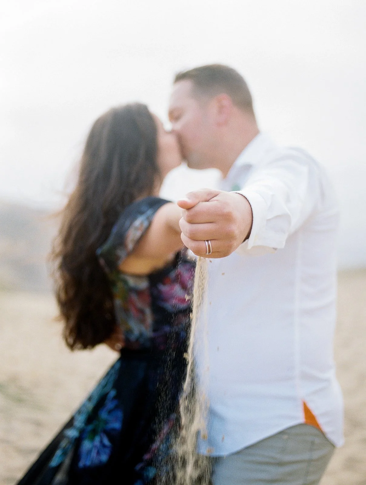 Couple kissing in soft focus while sand falls from hand in foreground, romantic Oregon Coast moment