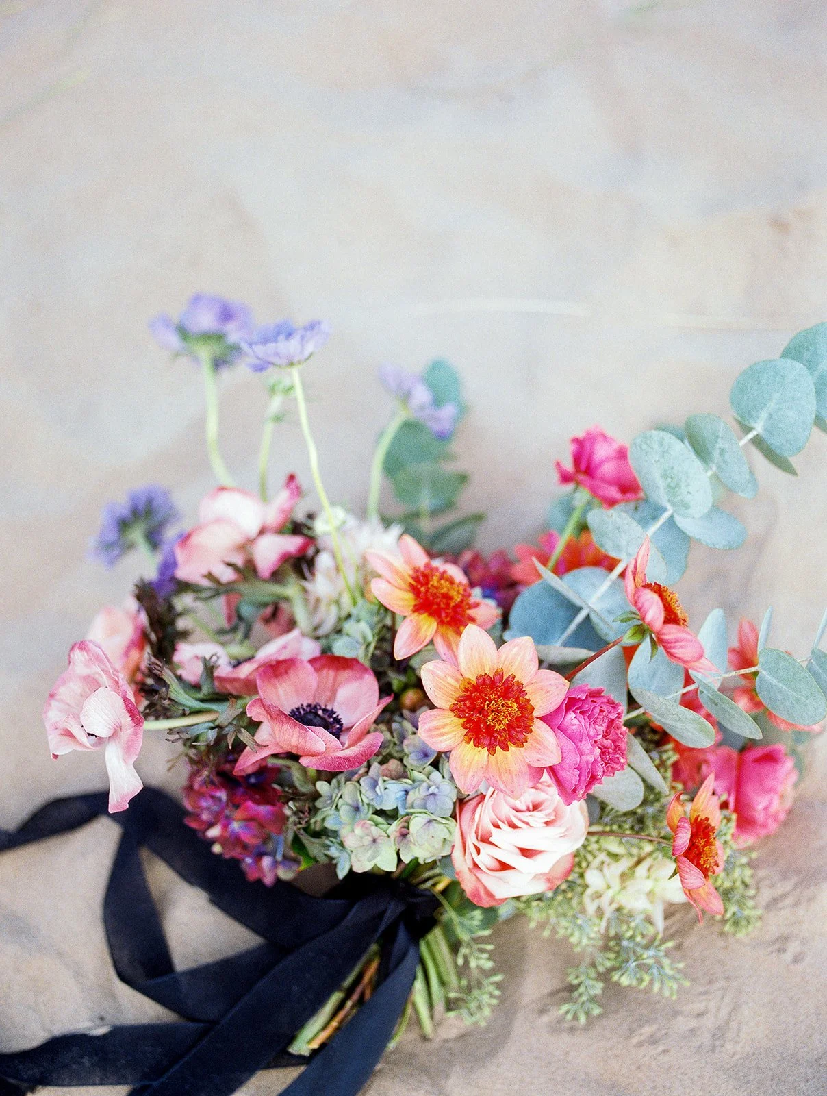 Close-up of vibrant bouquet with pink, coral, and greenery tones on sand, fine art wedding detail