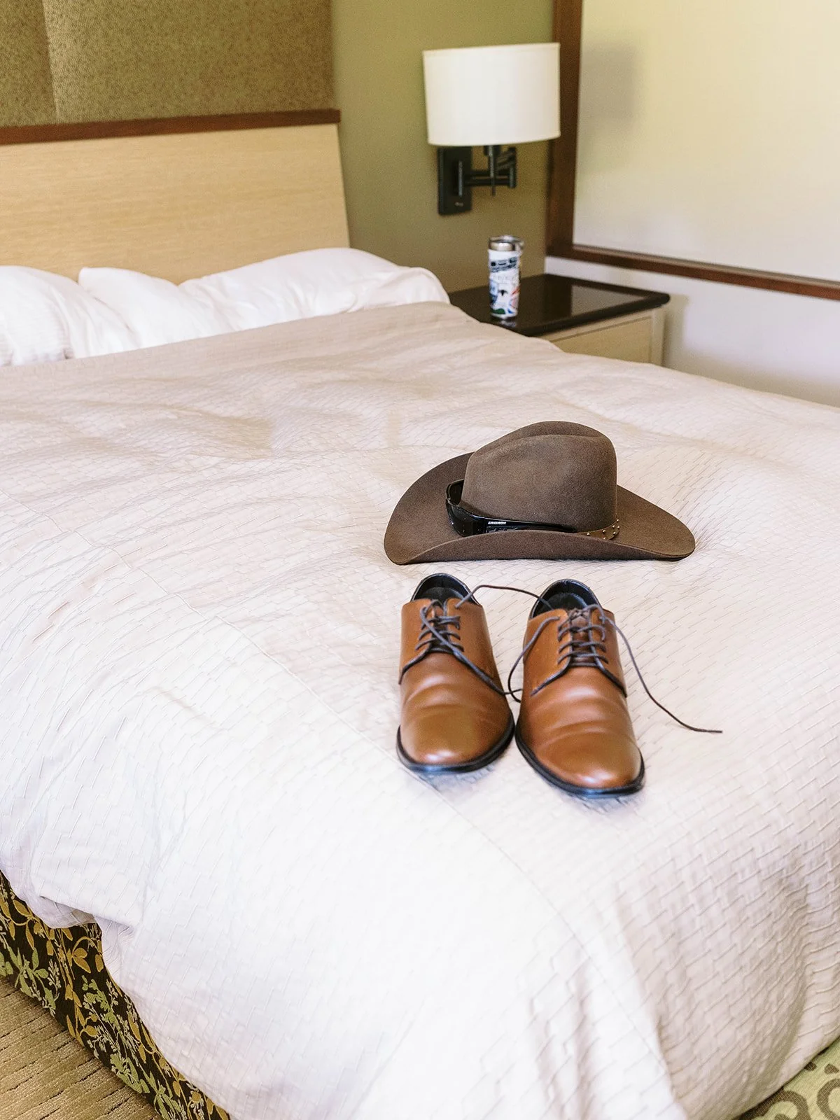 Brown dress shoes and hat arranged on bed in hotel room