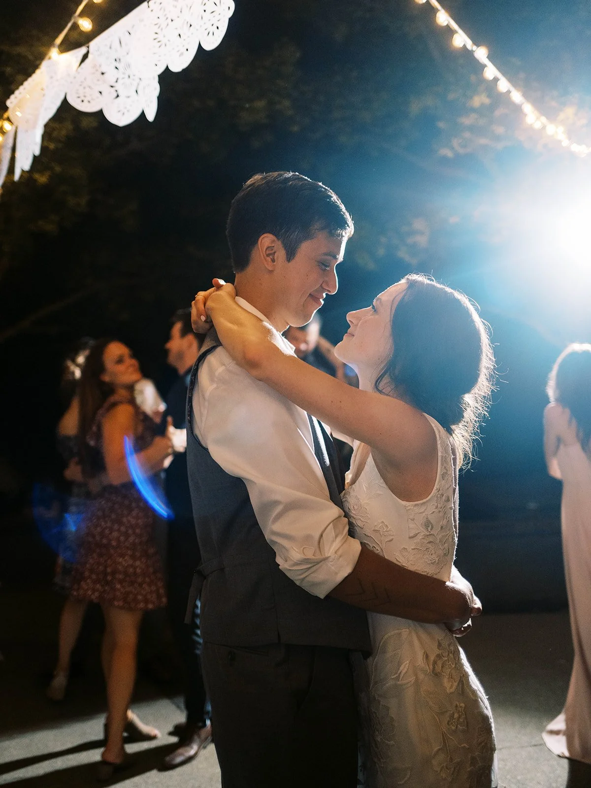Bride and groom dancing closely under string lights at nighttime outdoor wedding reception